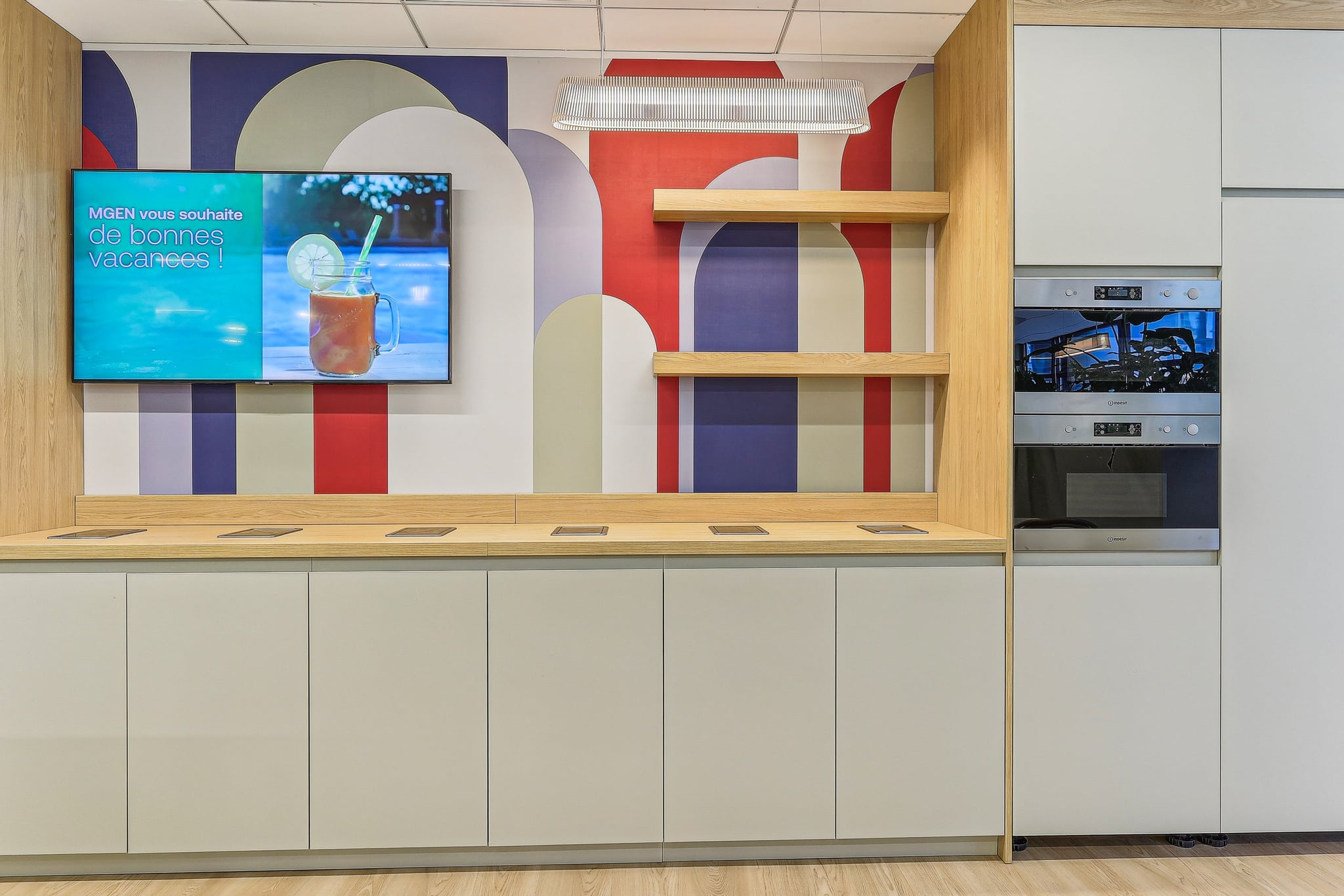 Kitchenette moderne avec papier peint graphique, écran MGEN de bonnes vacances et électroménager encastré.