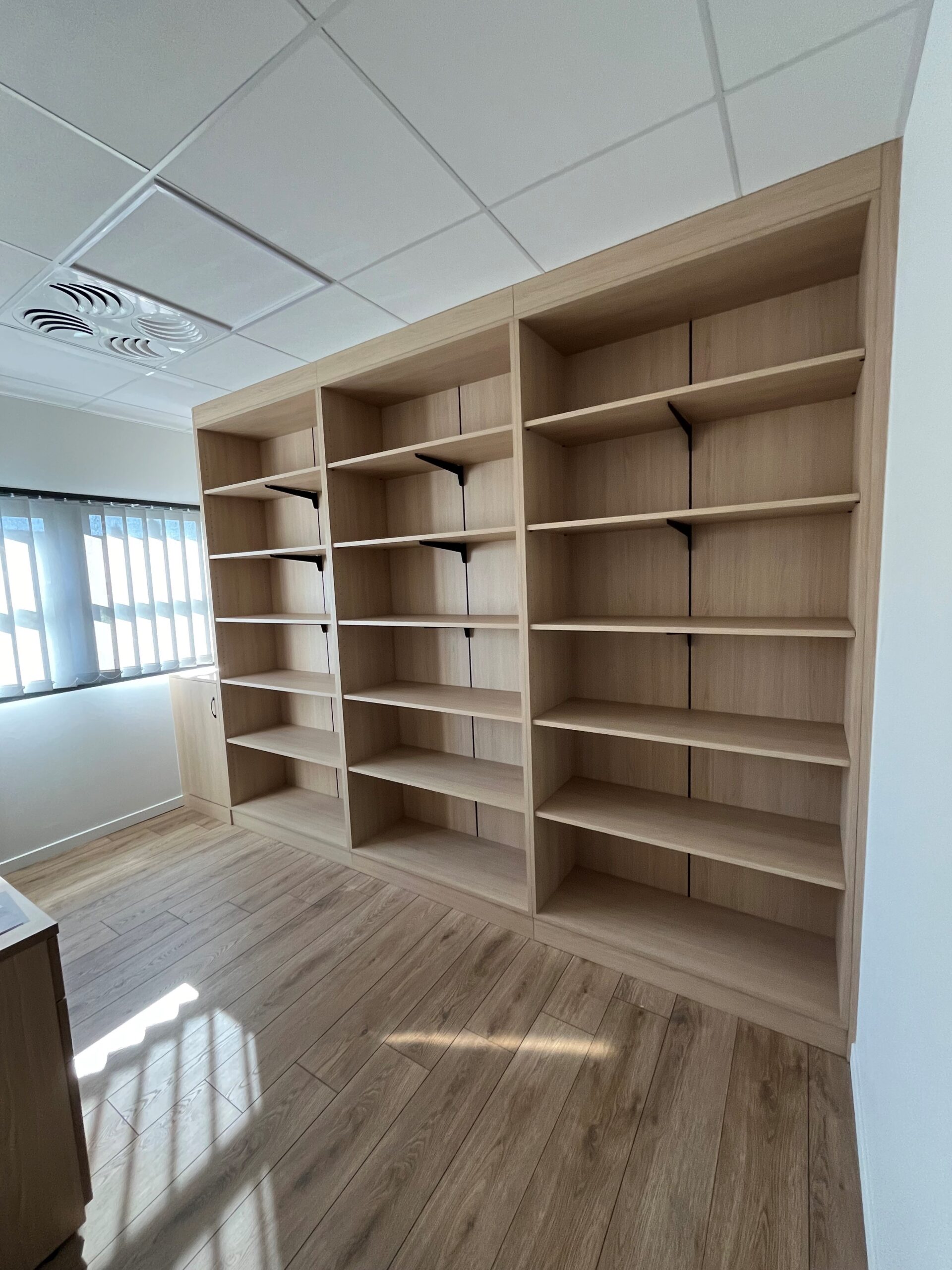 Bibliothèque murale en bois clair vide dans un bureau moderne avec parquet.