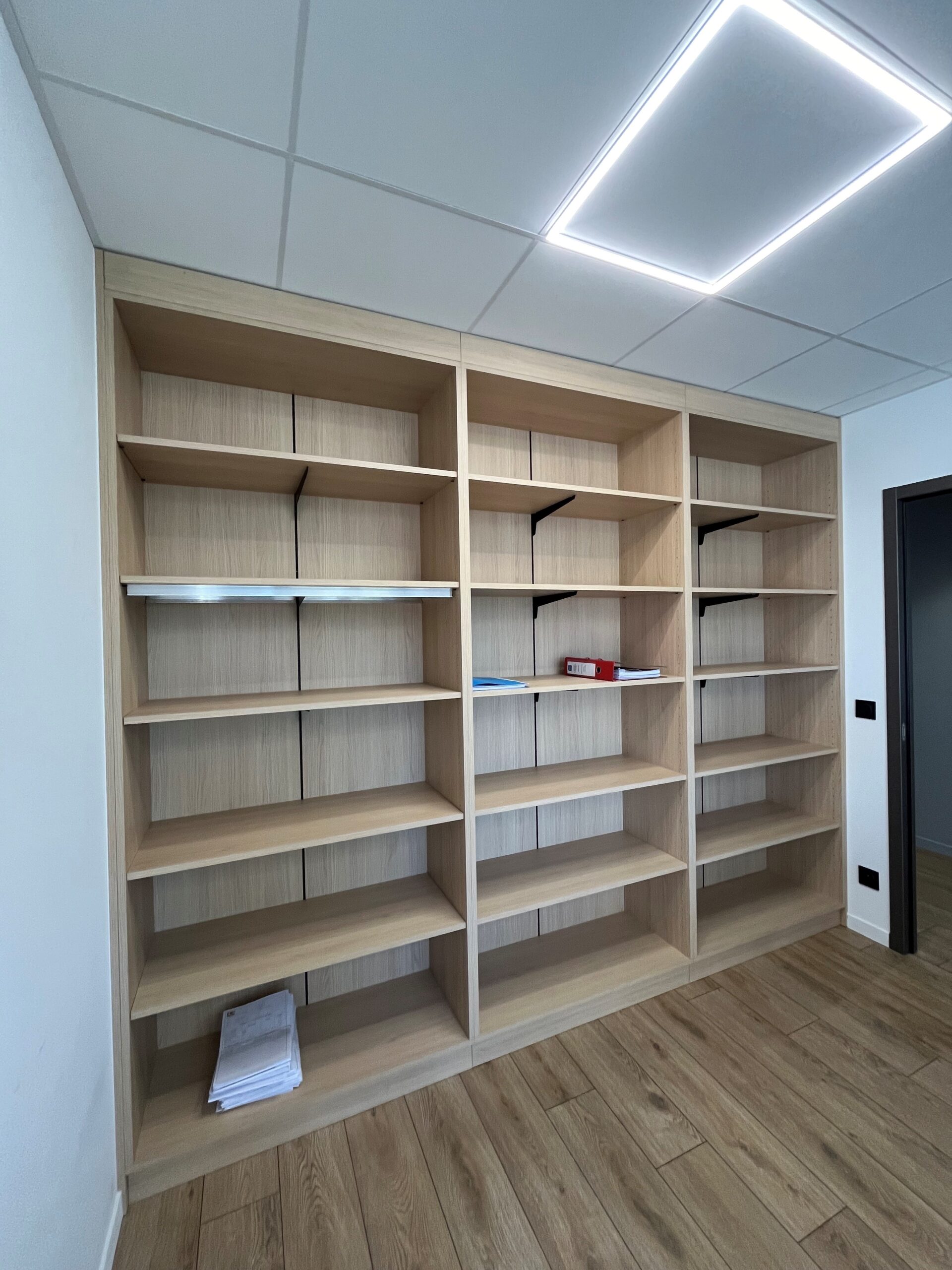 Bibliothèque sur mesure en bois clair pour bureau moderne Grande bibliothèque en bois clair, trois colonnes, bureau moderne avec éclairage LED au plafond.