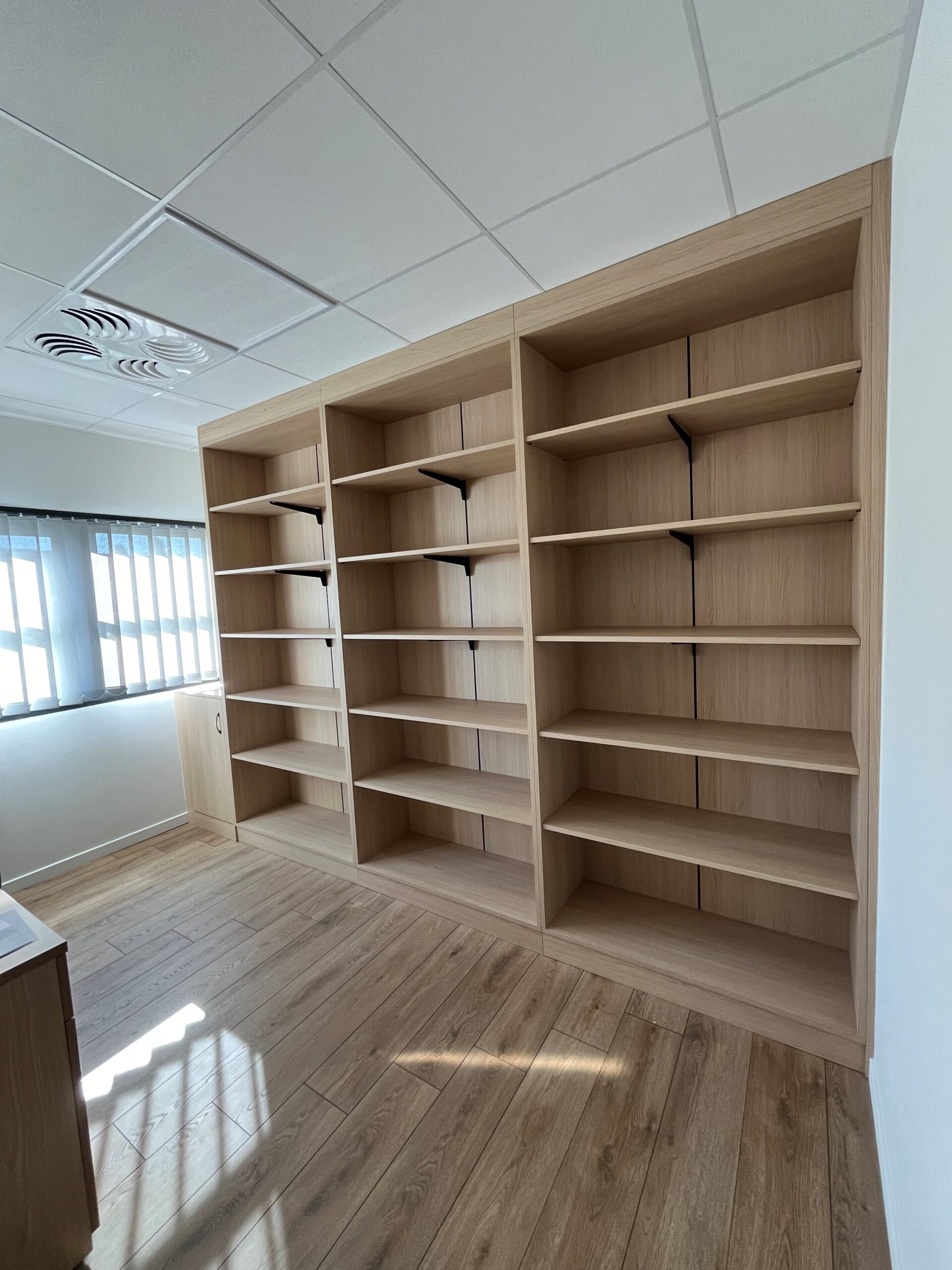 Grande bibliothèque en bois clair vide dans un bureau moderne.