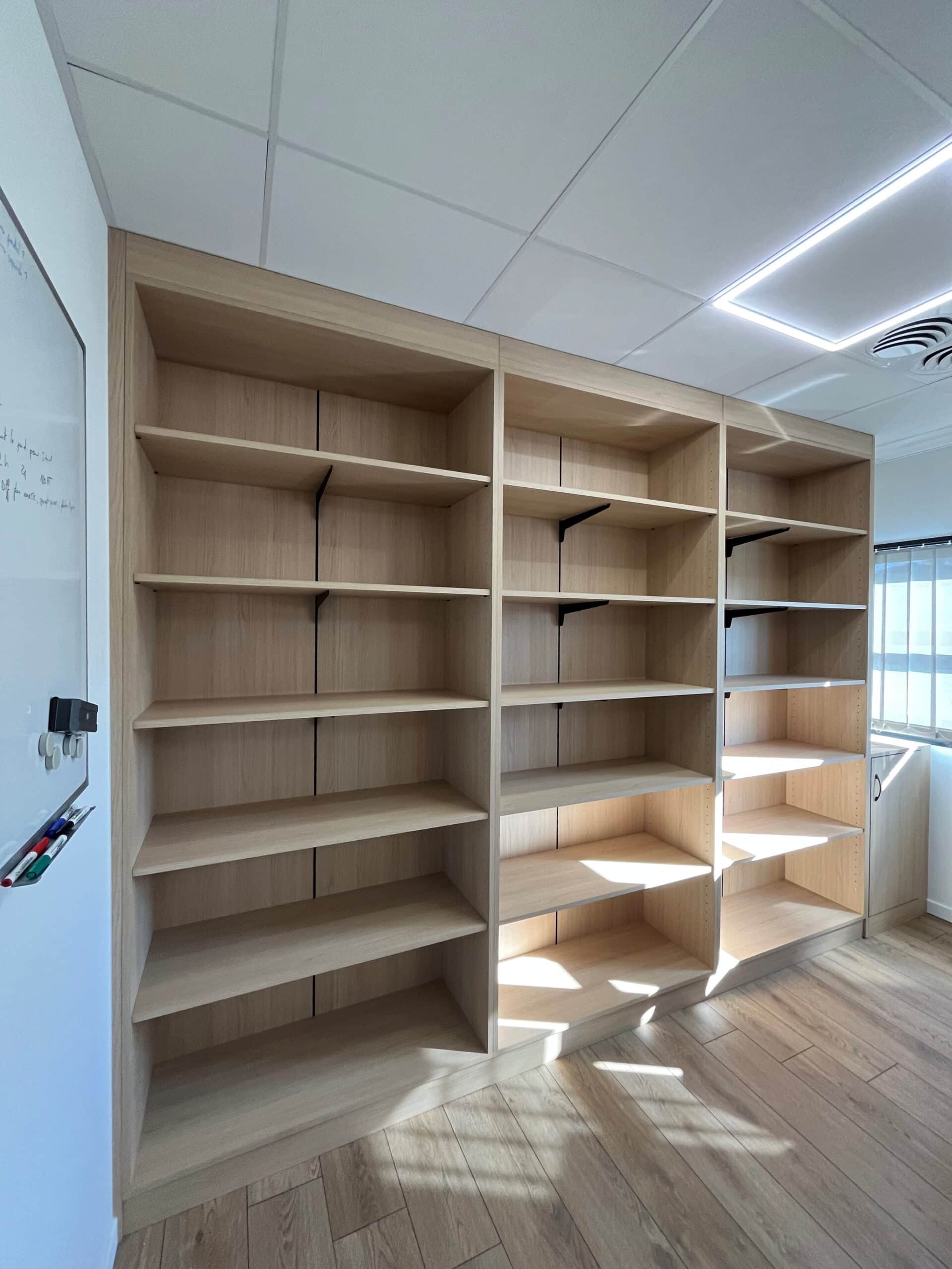 Bibliothèque murale en bois clair à trois sections et tableau blanc dans un bureau moderne.