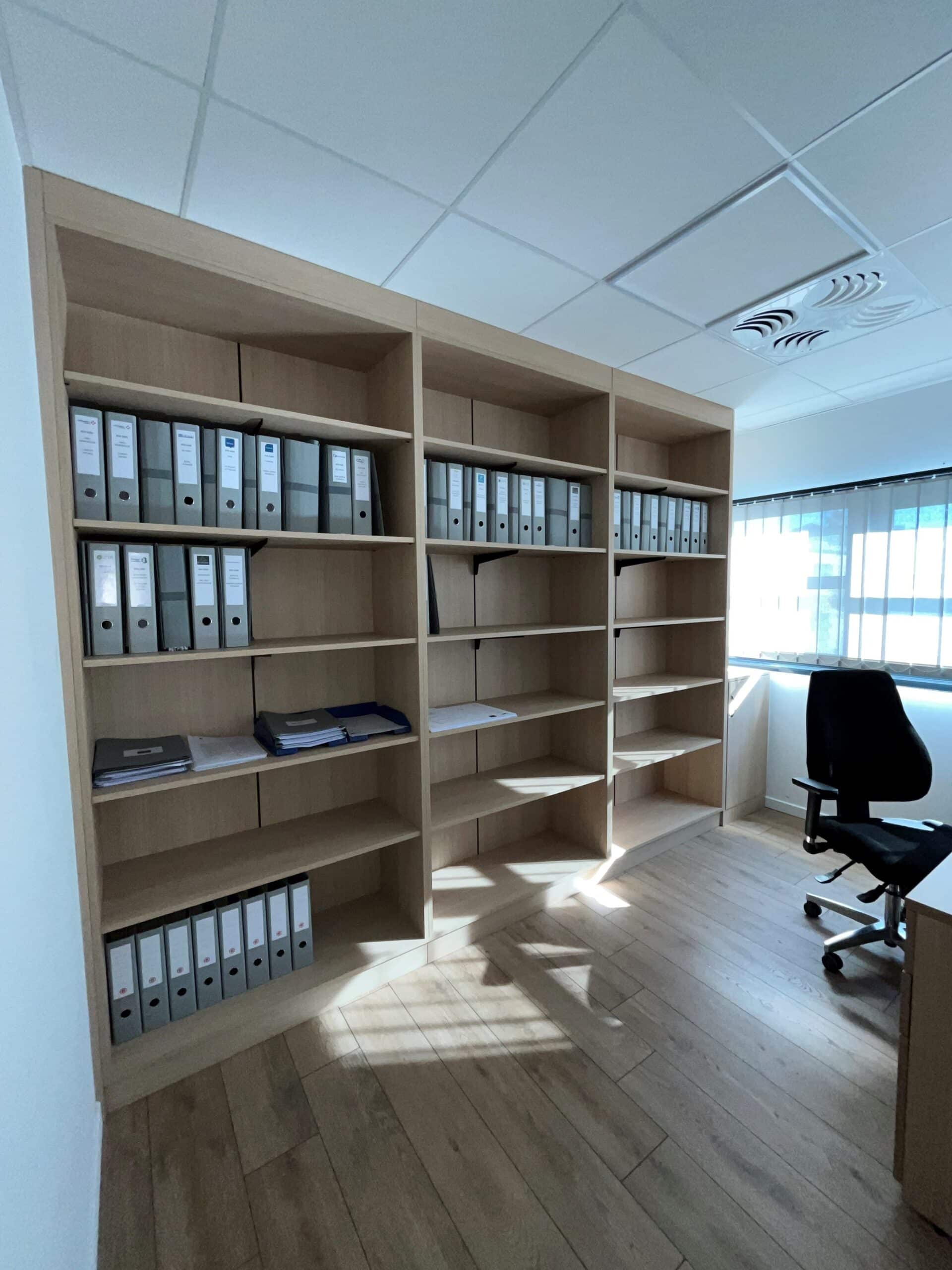 Grande bibliothèque en bois avec classeurs gris dans un bureau lumineux.