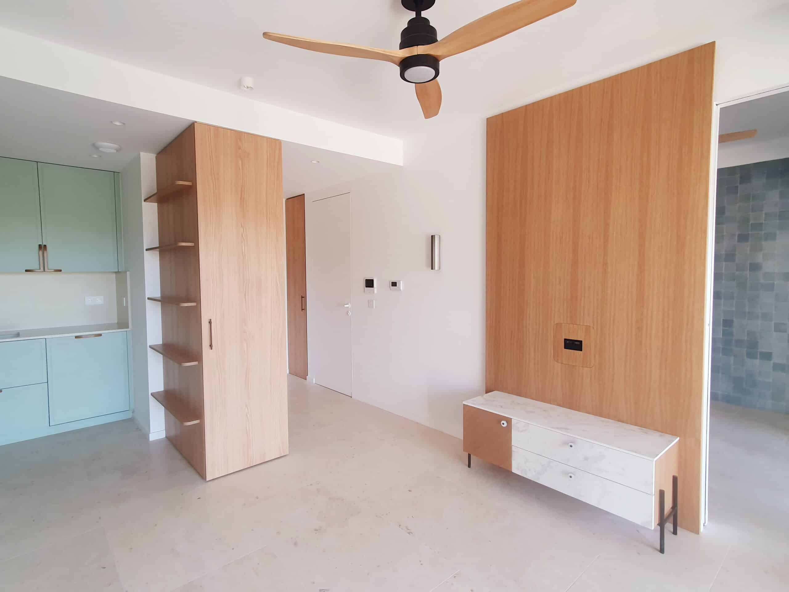 Intérieur moderne avec placards en bois clair, cuisine vert sauge et meuble TV en marbre élégant.
