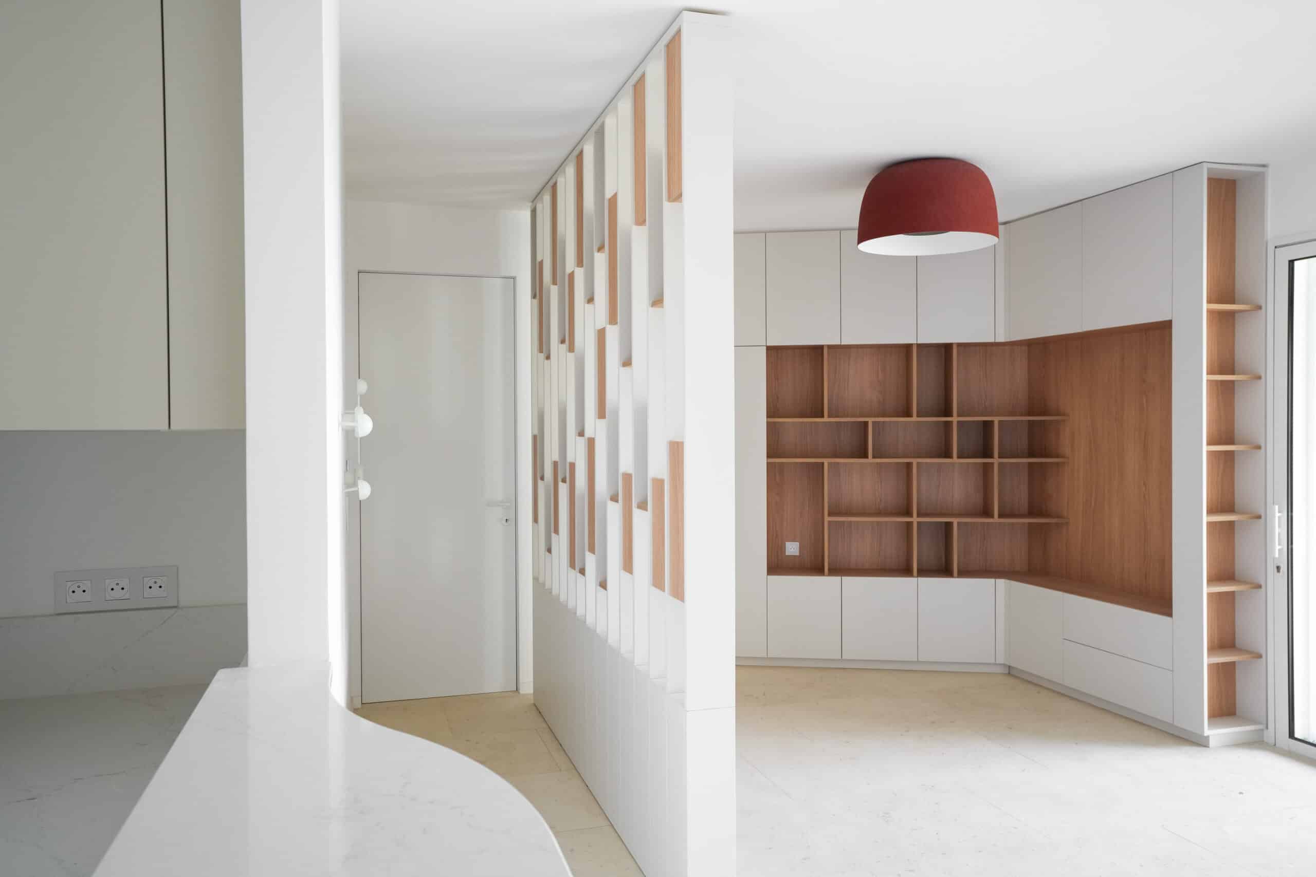 Cloison ajourée en bois et blanc séparant l'entrée d'un salon avec bibliothèque intégrée et luminaire rouge.