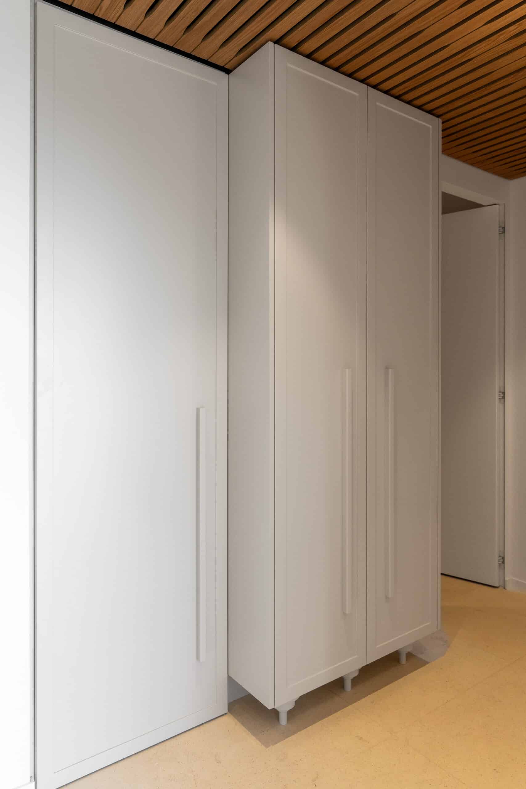 Armoire blanche moderne à poignées verticales sous un plafond à lattes de bois design.