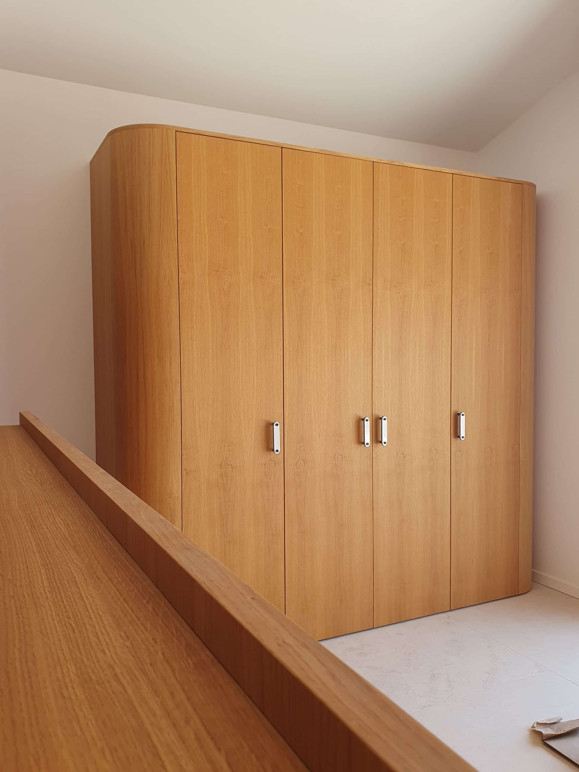 Placard sur mesure en bois clair avec finition arrondie et poignées métal dans un intérieur minimaliste.