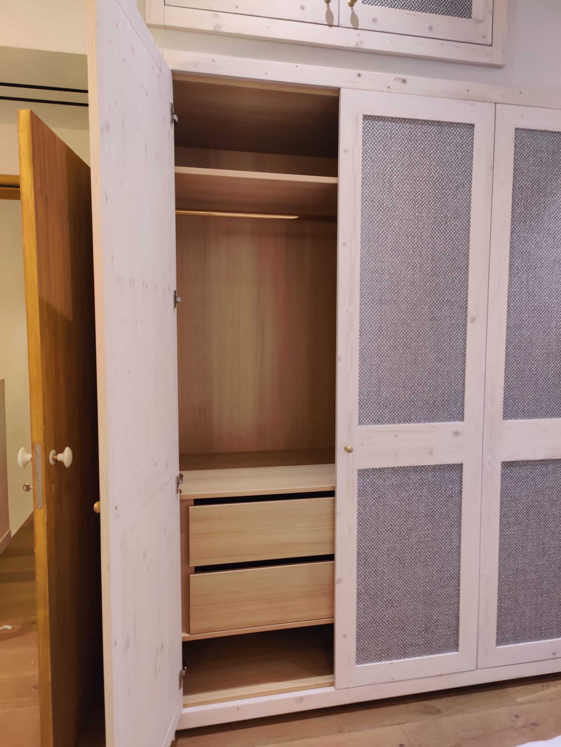 Armoire en bois clair ouverte dévoilant des étagères et tiroirs, avec portes à motifs tressés gris.