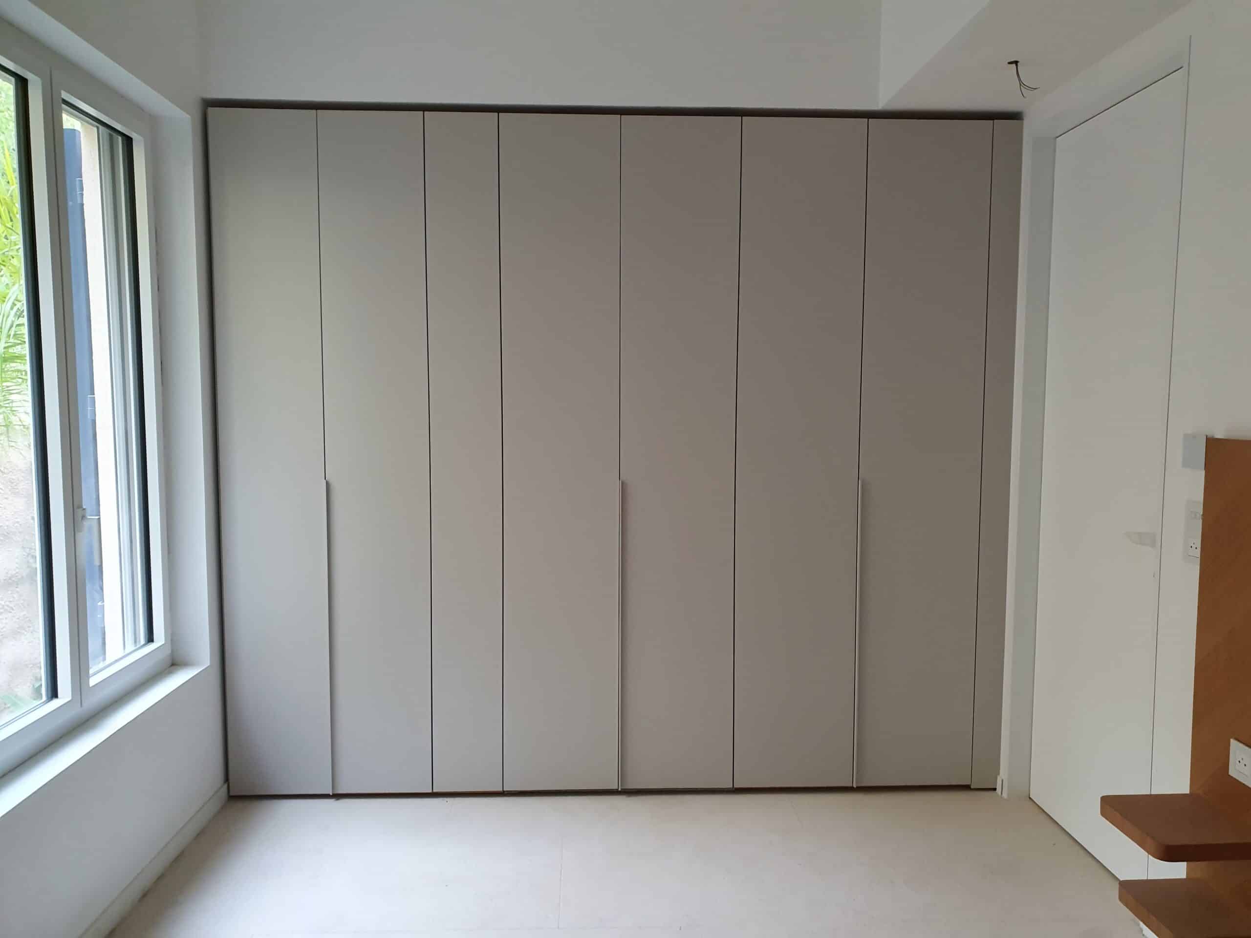 Armoire encastrée minimaliste beige clair, huit portes sur mesure dans une chambre lumineuse.