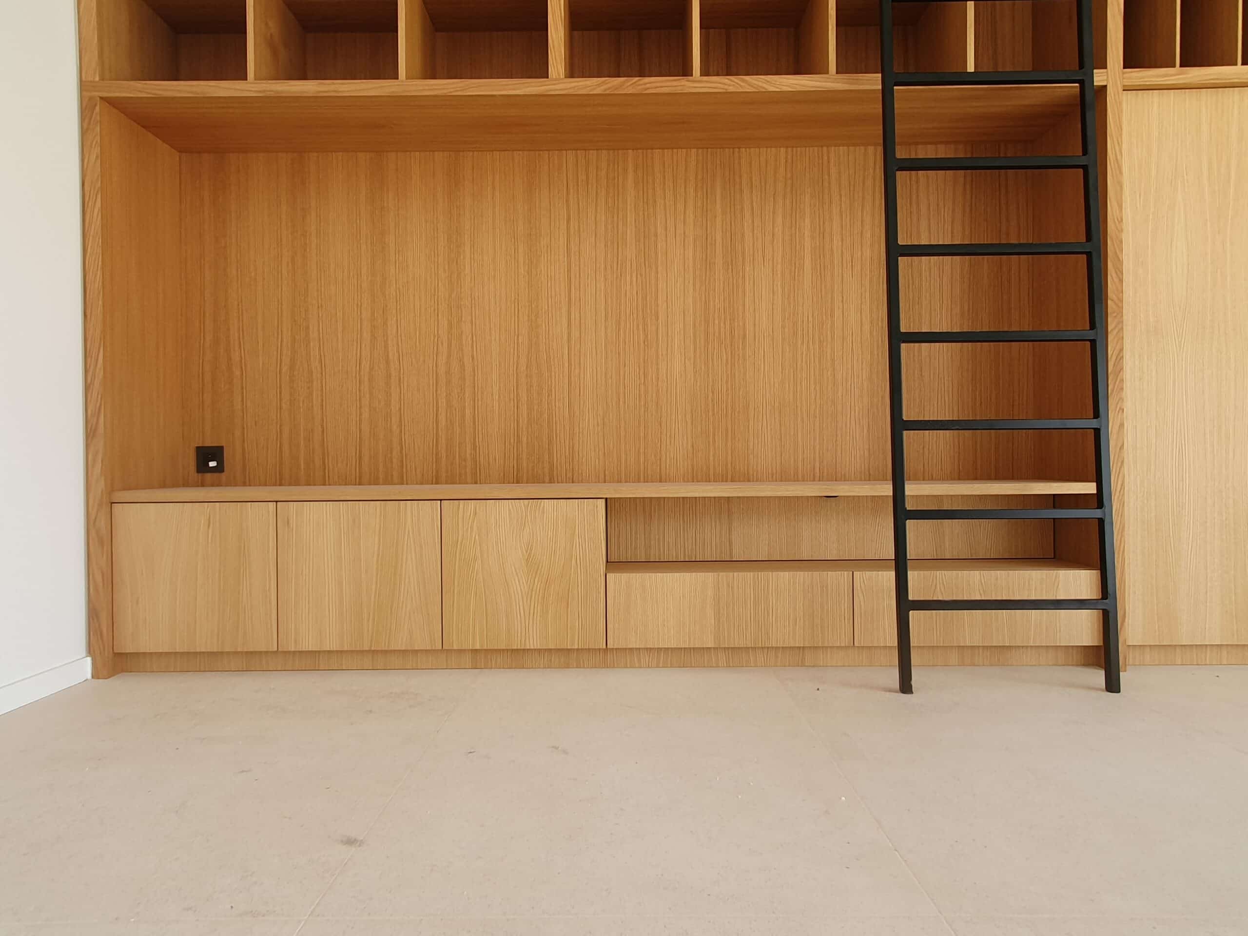 Bibliothèque en bois clair avec échelle noire coulissante et rangements intégrés minimalistes.