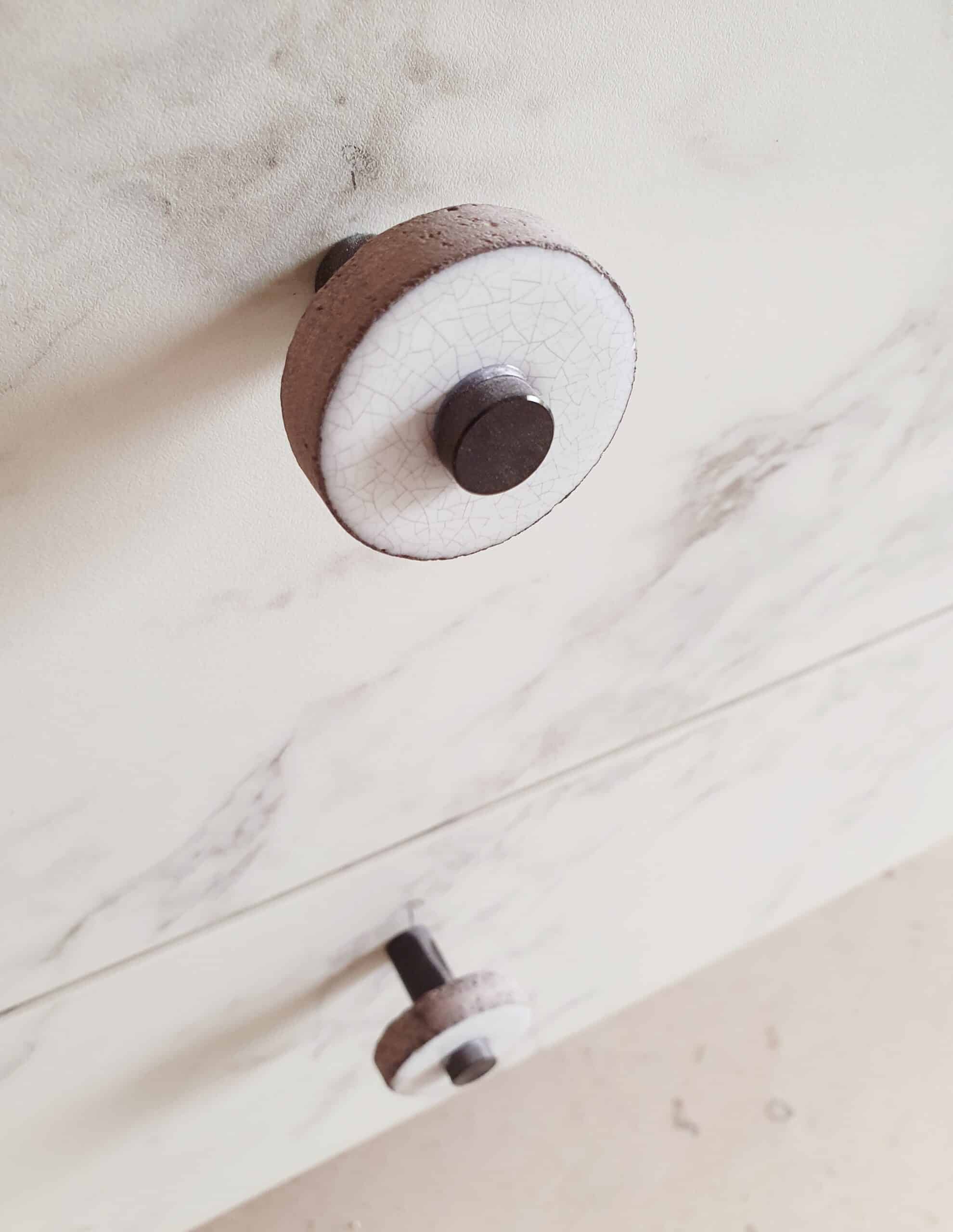 Bouton de tiroir rond en céramique craquelée et métal sur un meuble imitation marbre blanc.