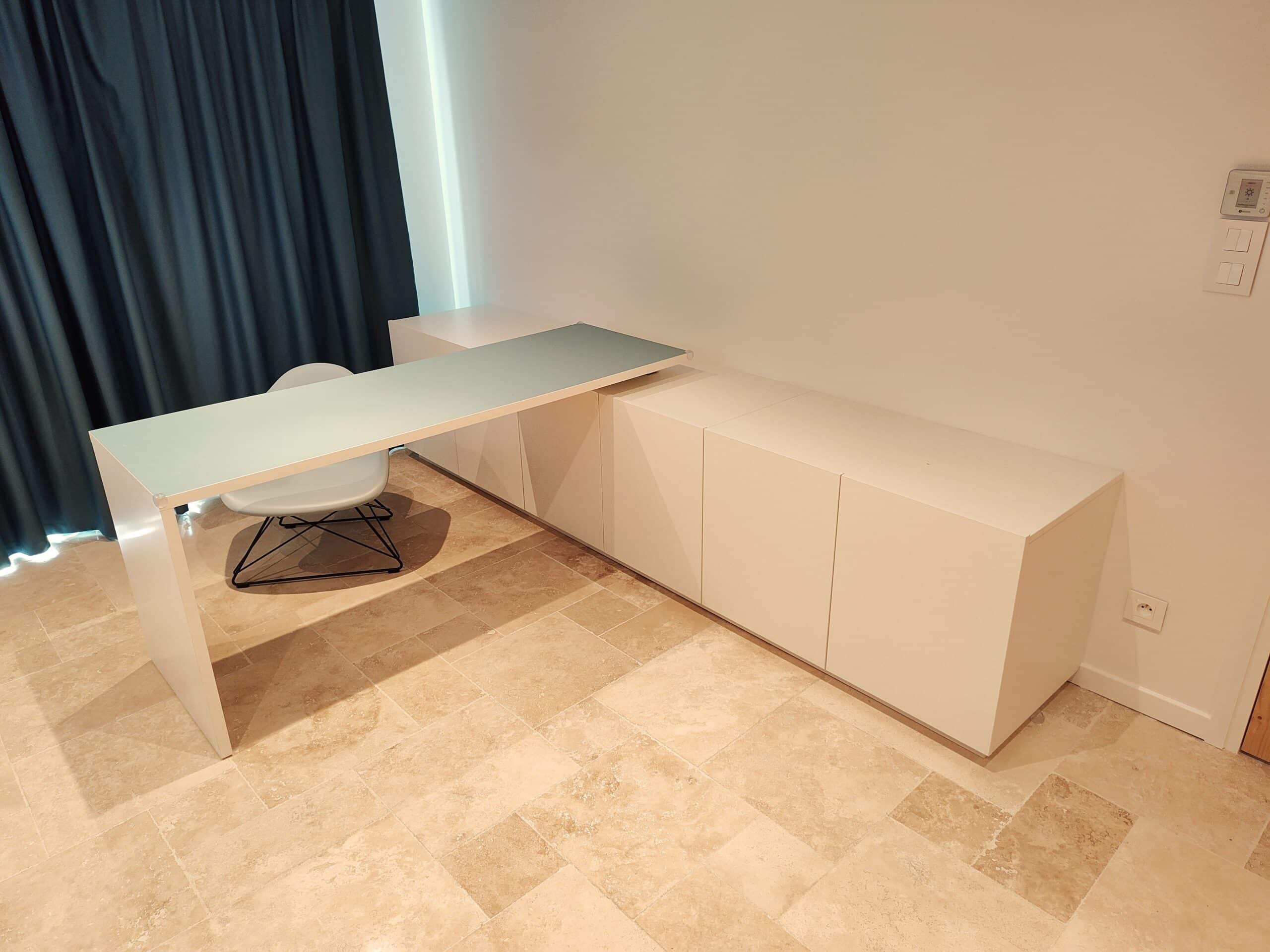 Bureau blanc moderne, plateau verre et rangement bas sur sol en pierre claire.