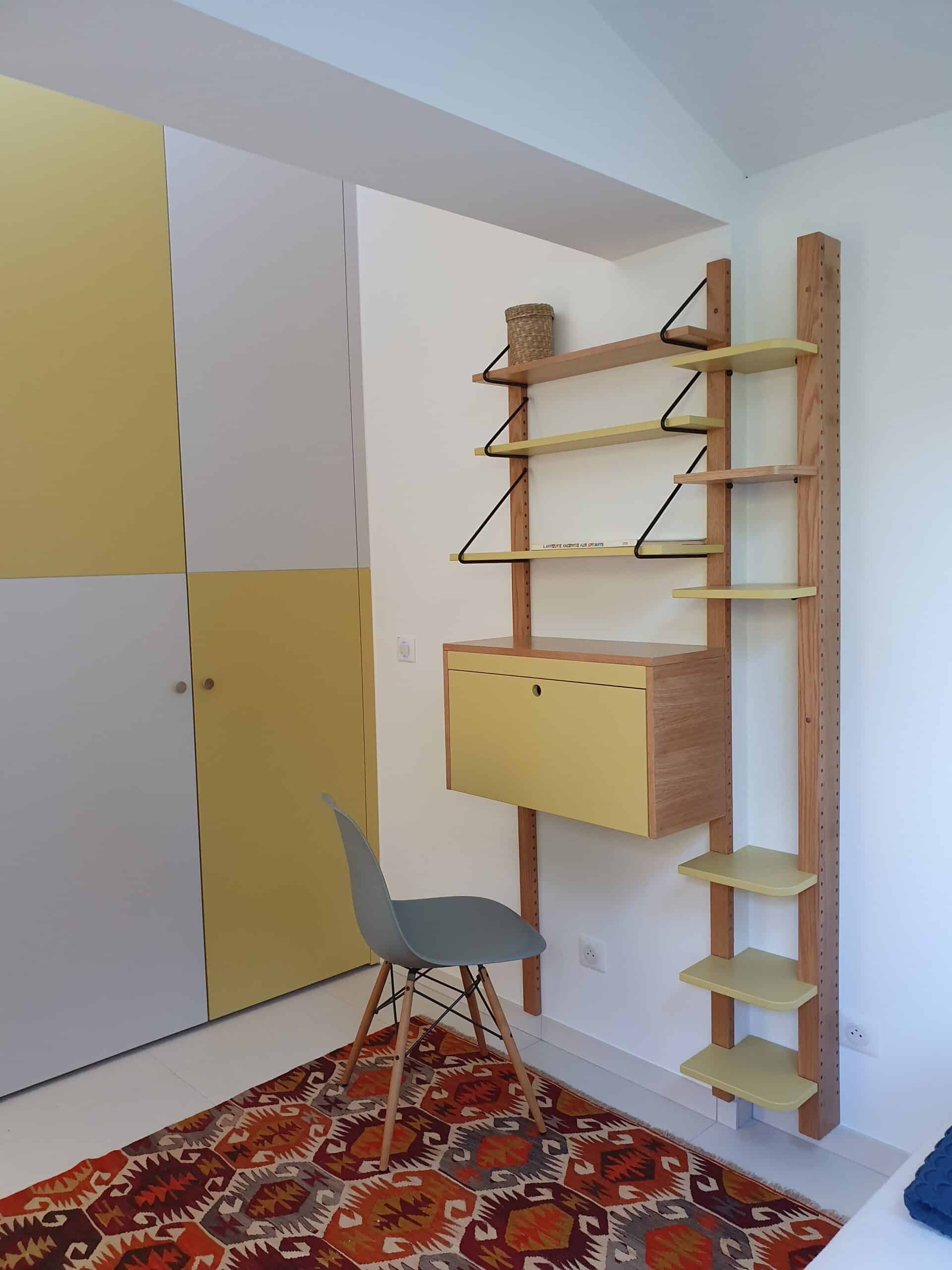 Bureau mural bois et jaune, étagères modulables, chaise grise et tapis à motifs géométriques.