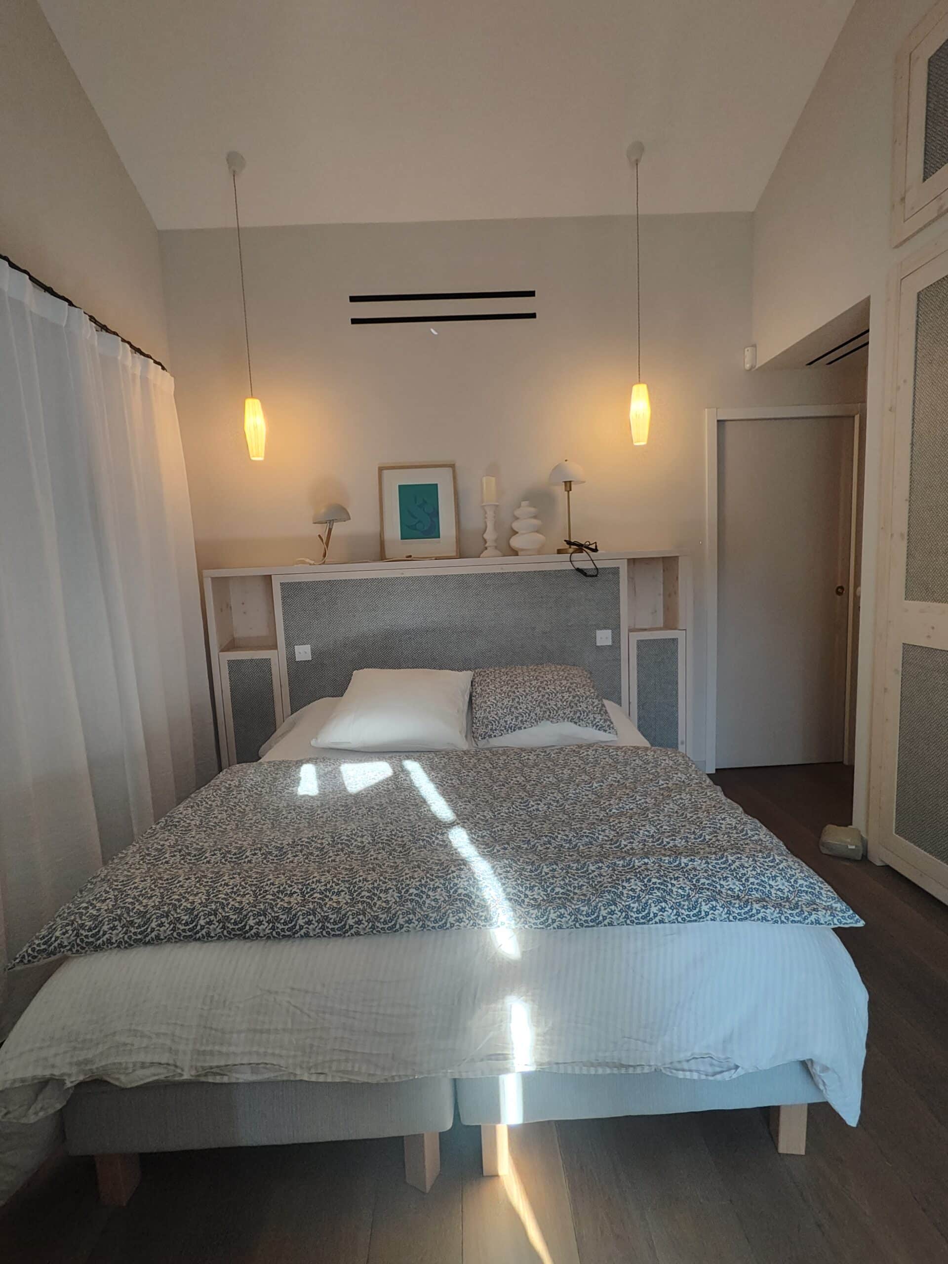Chambre moderne avec lit à motifs bleus, suspensions design et tête de lit à niches intégrées.