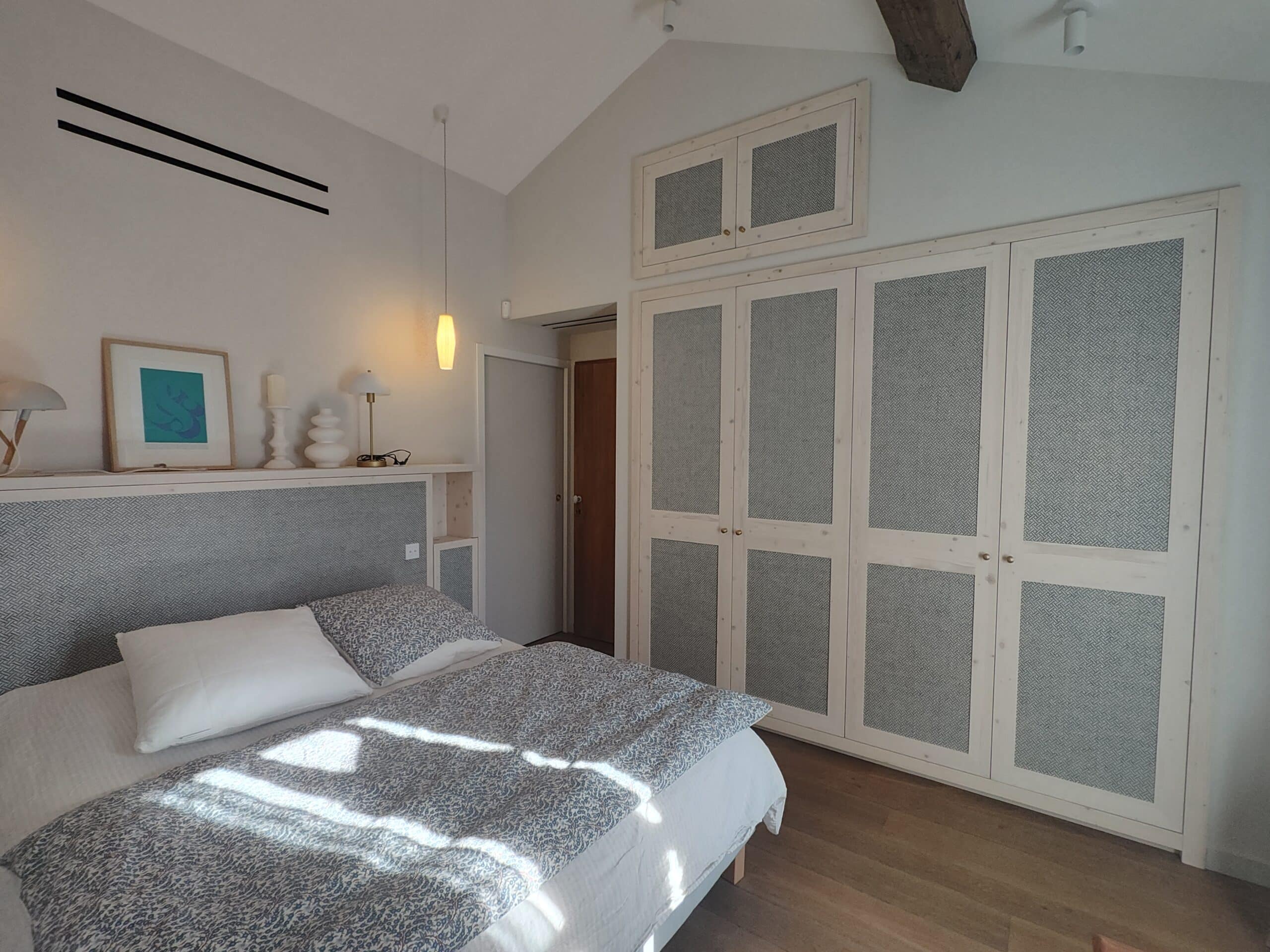 Chambre lumineuse, lit bleu et blanc, placards intégrés texturés et décoration épurée sous plafond mansardé.