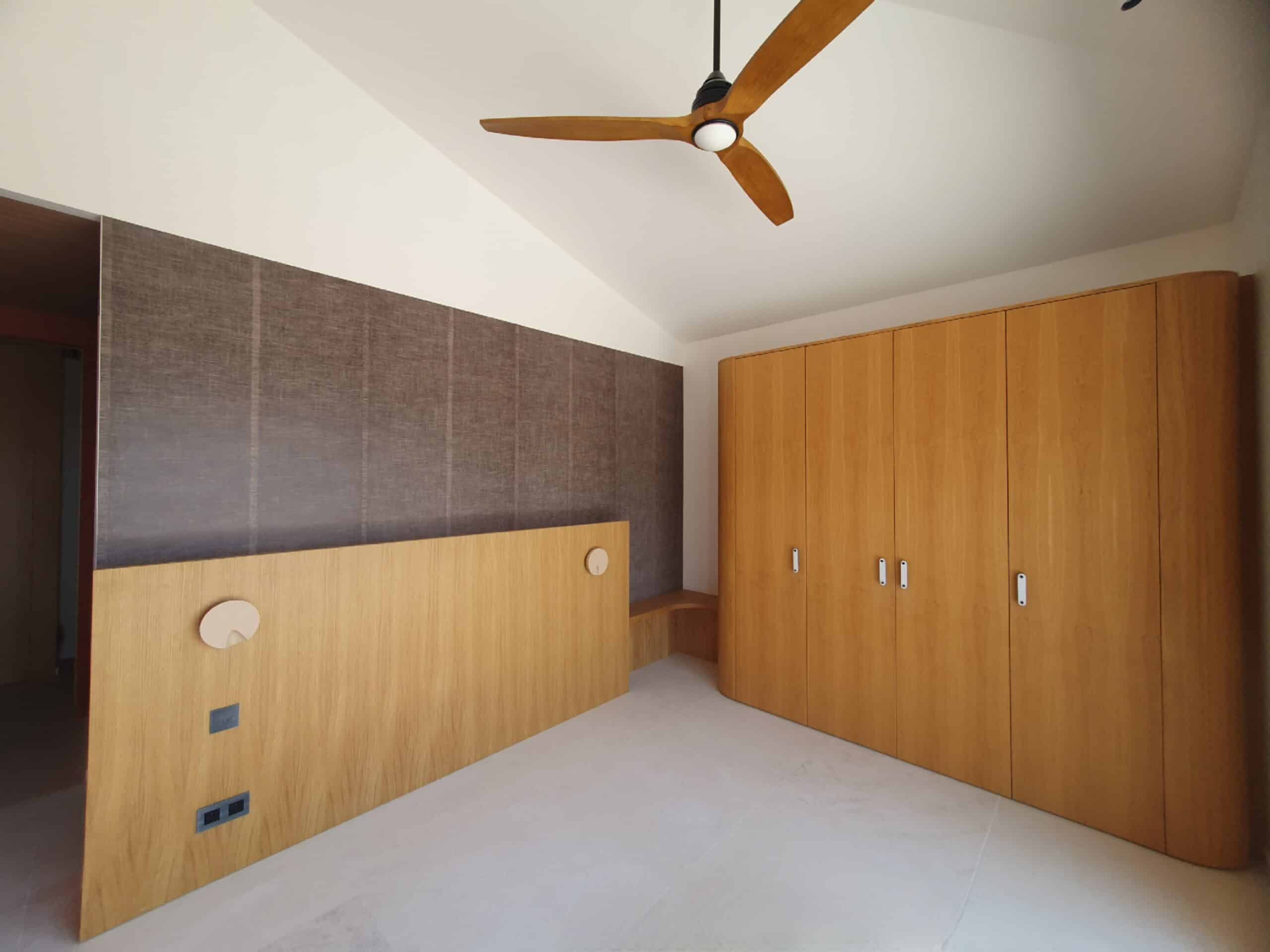 Chambre moderne avec grand placard en bois clair, ventilateur de plafond et tête de lit épurée intégrée.