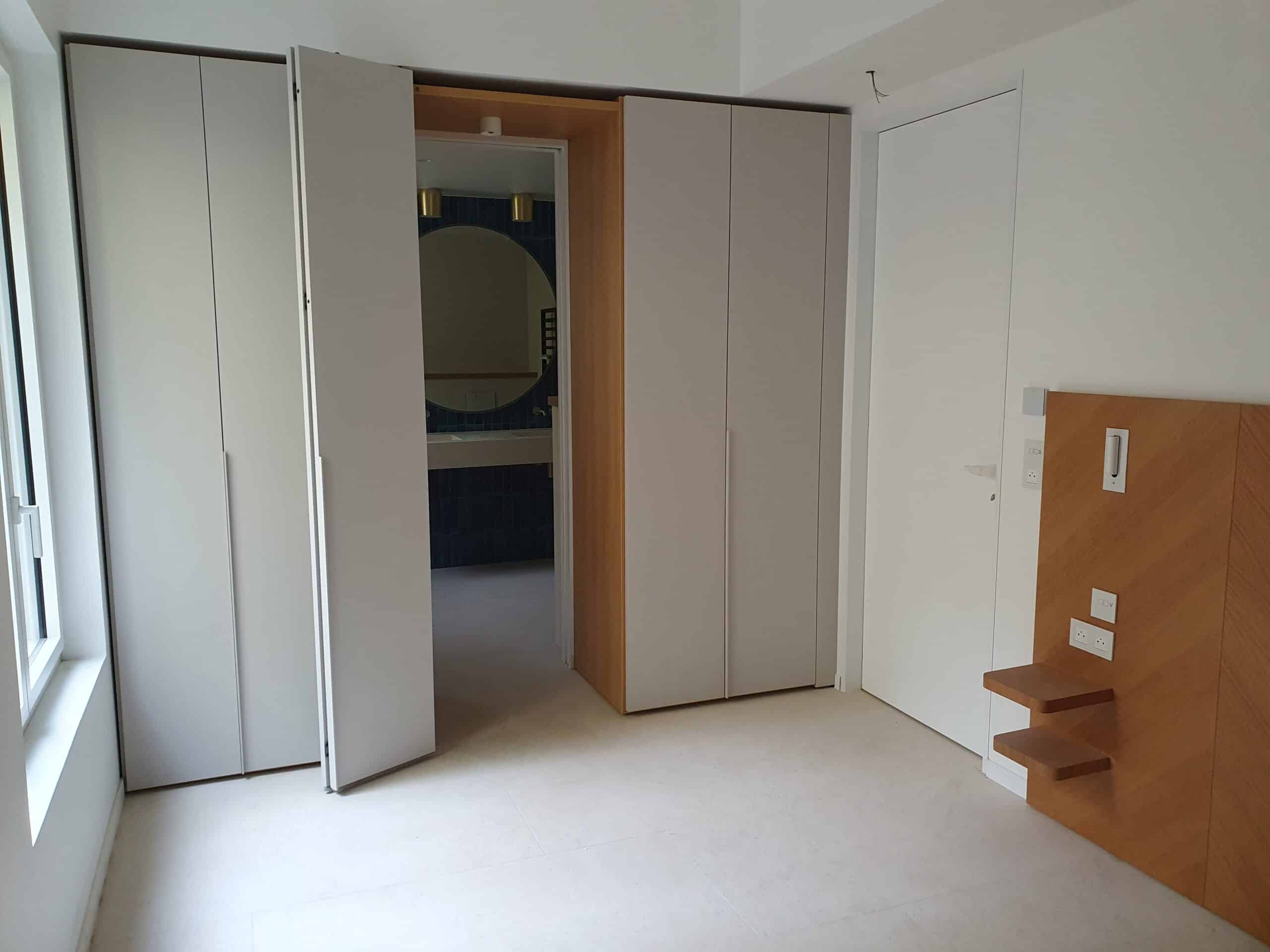 Armoire grise, passage vers salle de bain bleue et tête de lit boisée dans une chambre moderne.