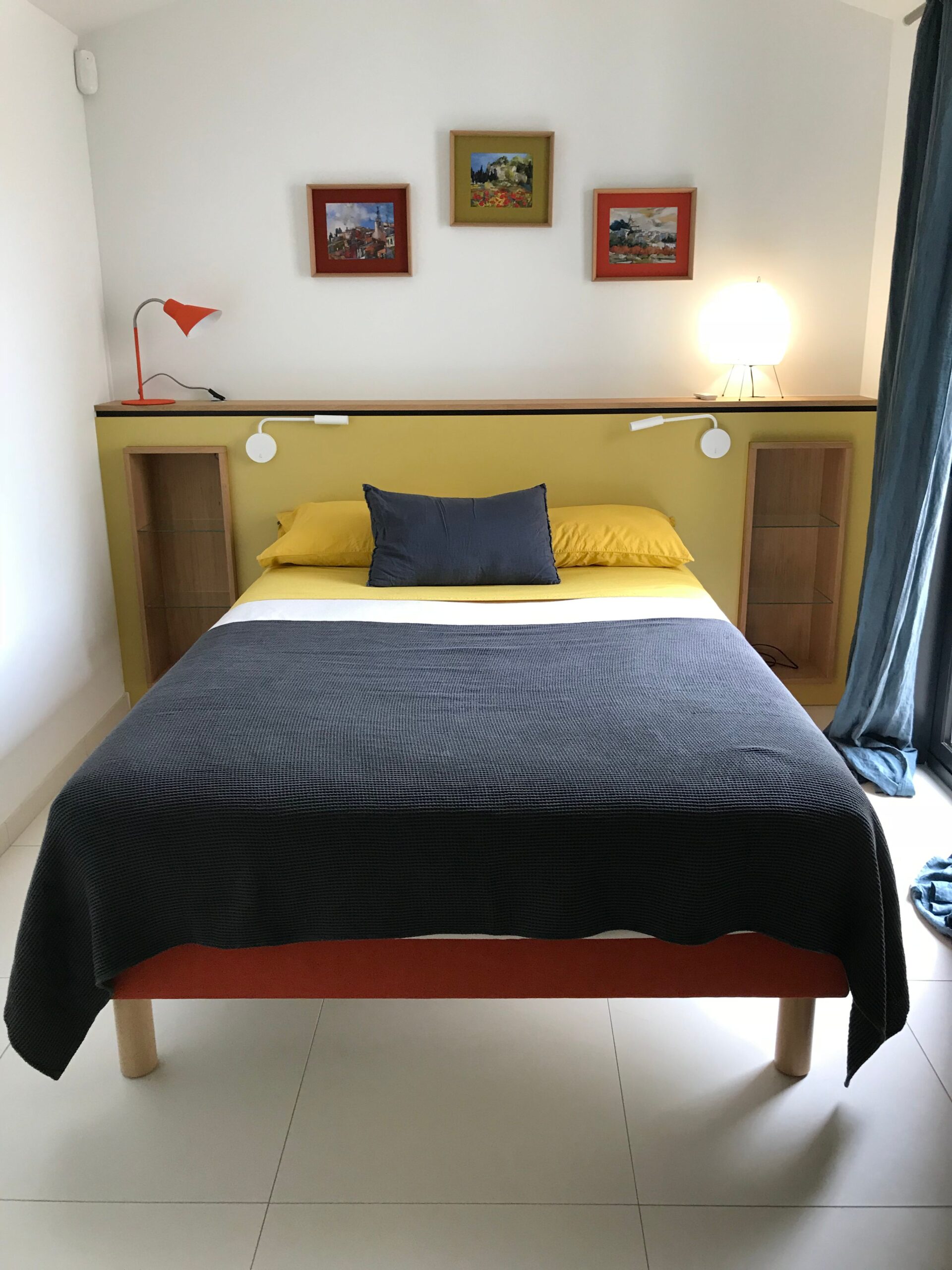 Chambre moderne : tête de lit jaune, couvre-lit gris anthracite, cadres d'art et lampes design colorées.
