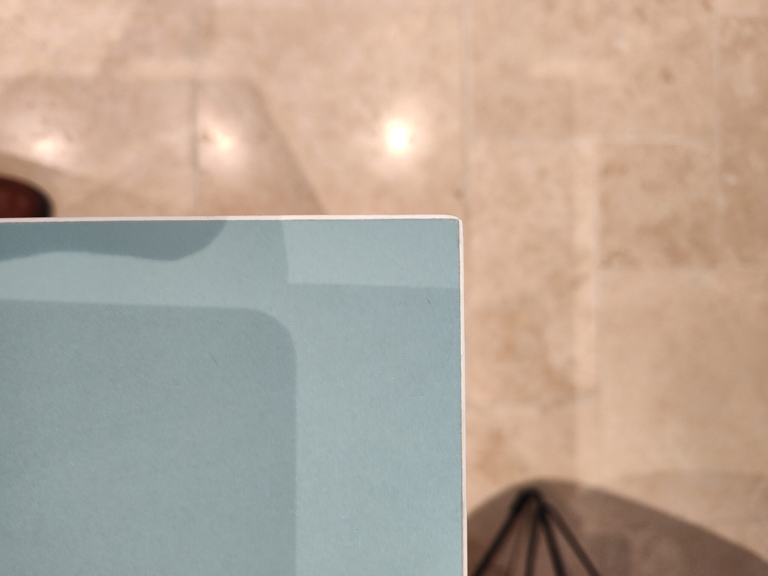 Coin supérieur droit d'un livre bleu ciel posé sur un carrelage beige flou.