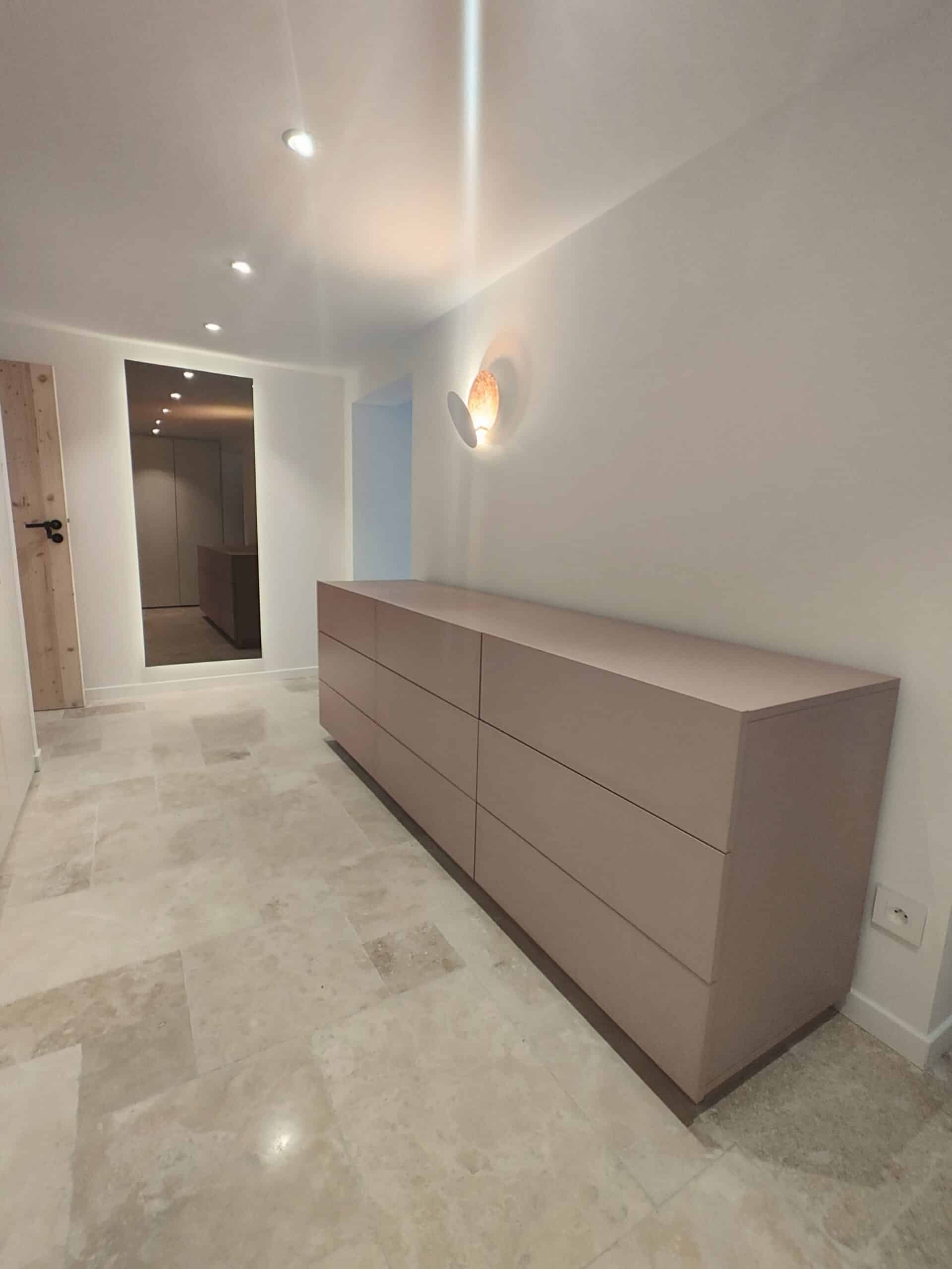 Commode mauve, sol en pierre et miroir dans un couloir moderne épuré.