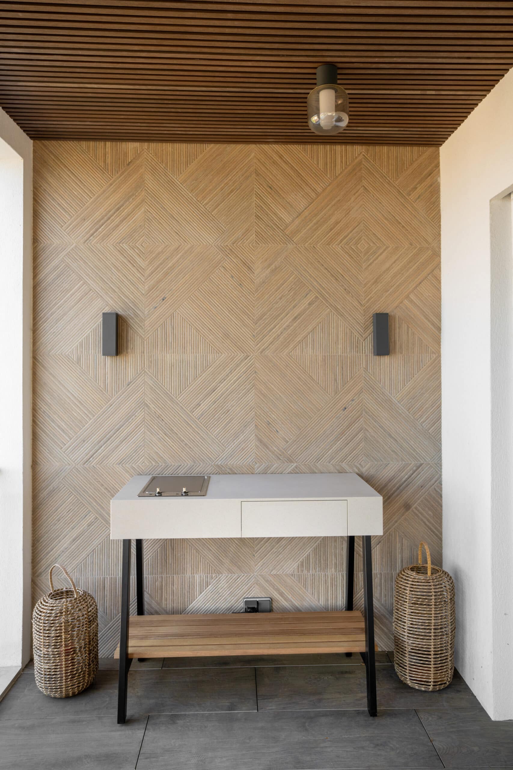 Cuisine d'extérieur moderne avec barbecue encastré, mur en bois géométrique et paniers en osier sur une terrasse.