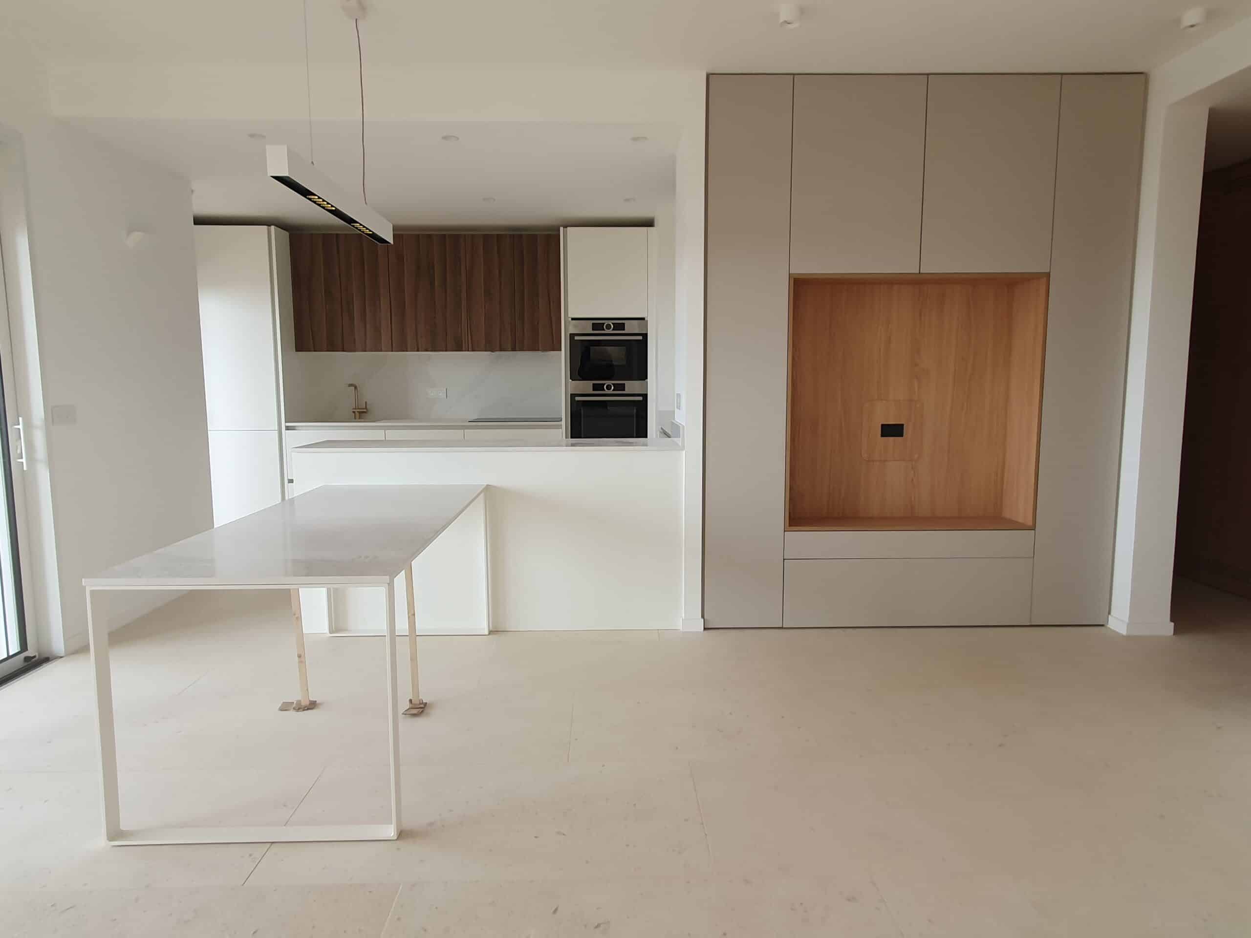 Cuisine moderne minimaliste avec îlot blanc, meubles en bois et électroménagers intégrés.