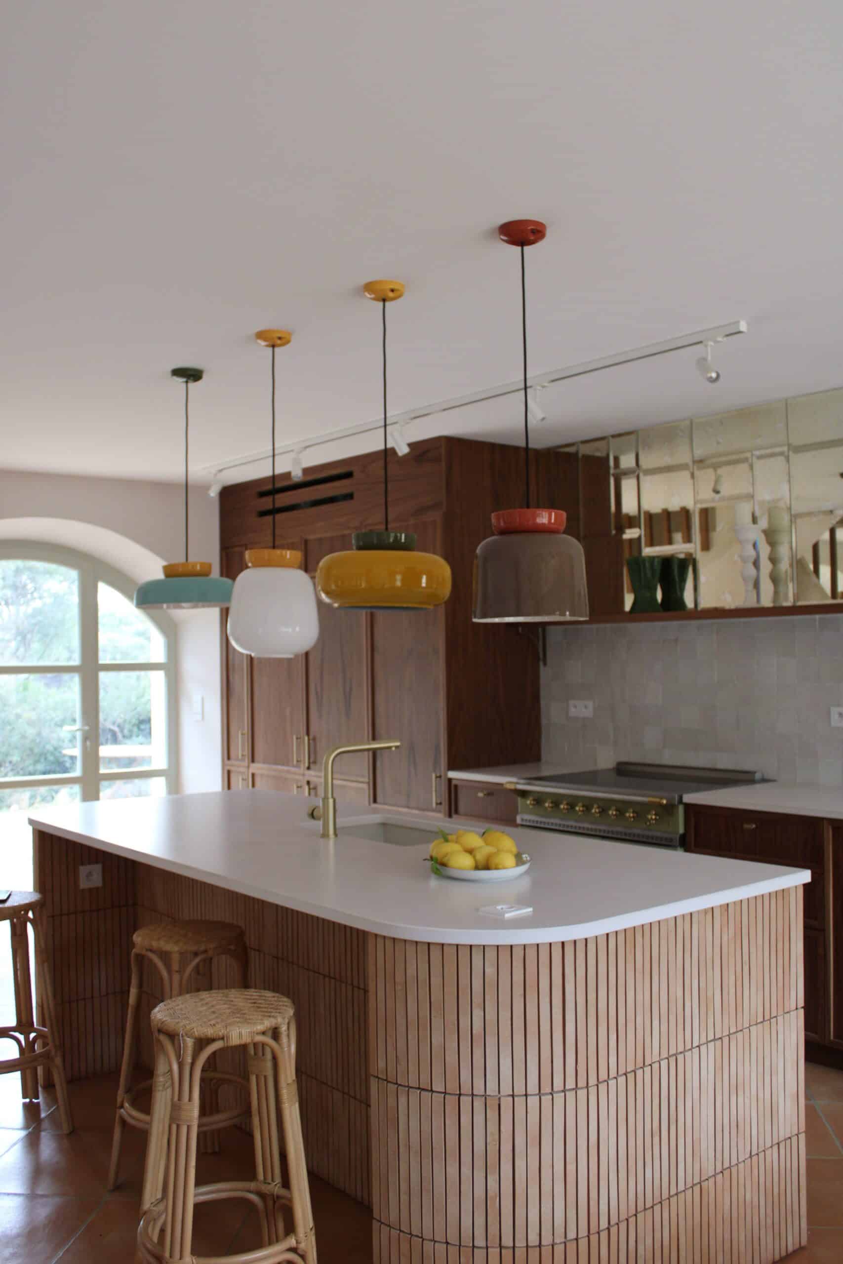 Cuisine moderne avec îlot en bois, suspensions colorées et tabourets en rotin.