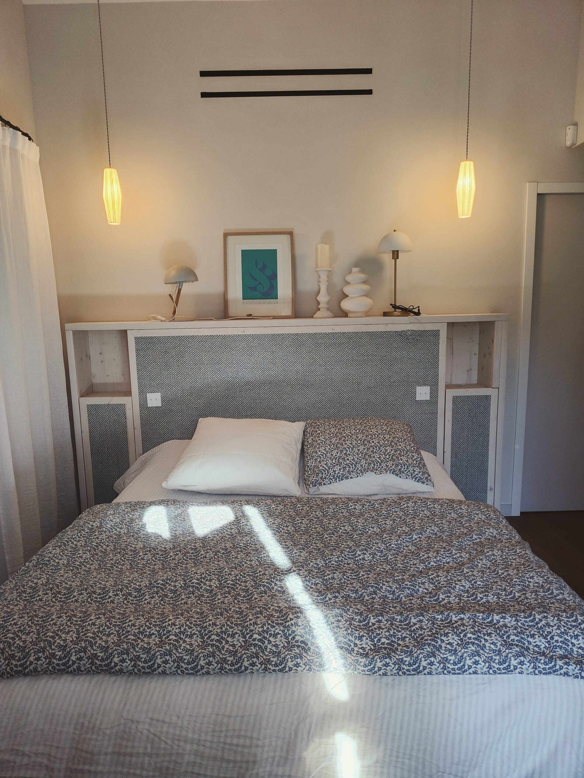 Chambre épurée : lit à motifs bleus, tête de lit avec étagère déco et luminaires suspendus chaleureux.