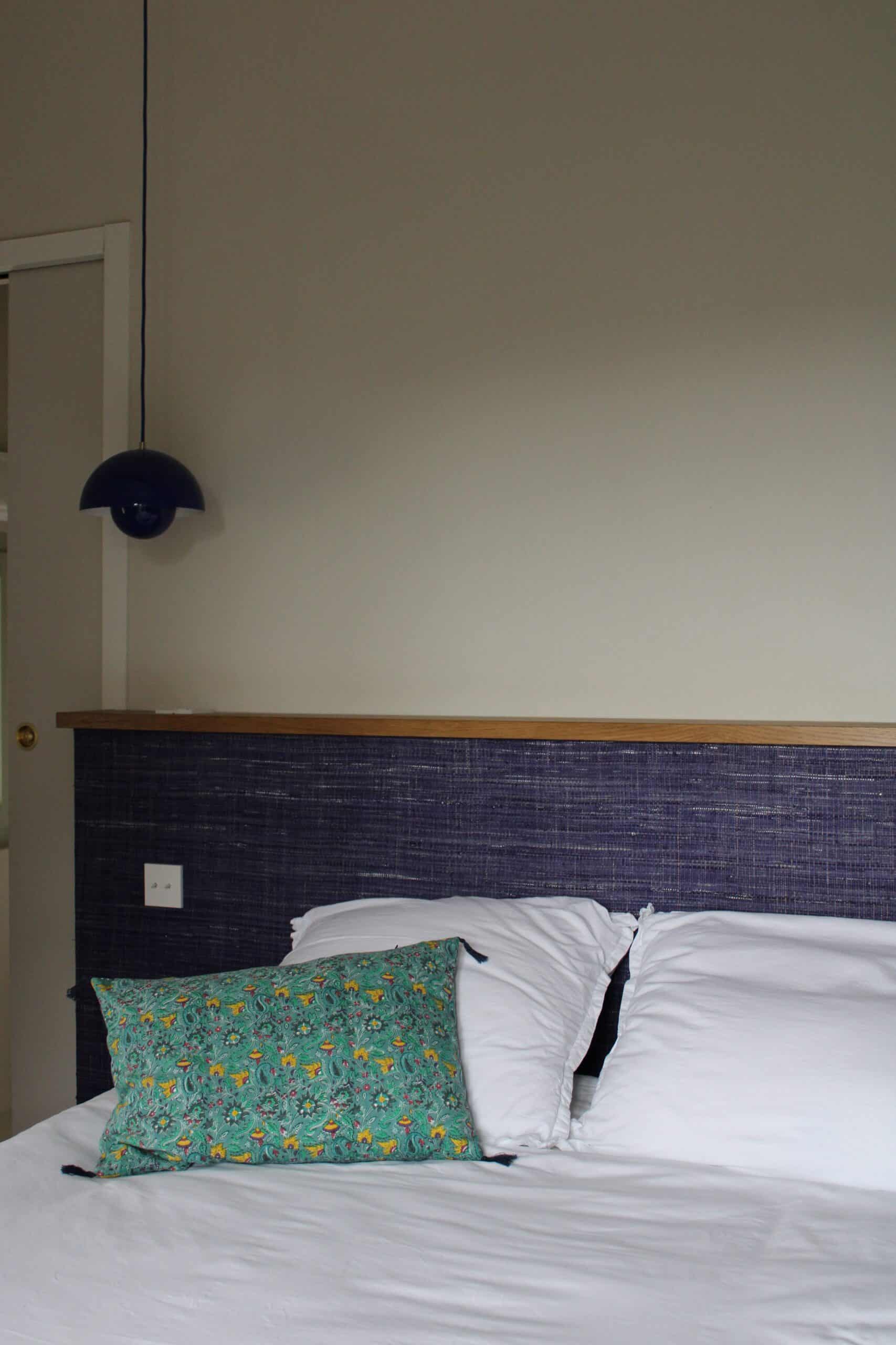 Chambre avec lit blanc, tête de lit bleue, coussin vert à motifs et luminaire suspendu design.