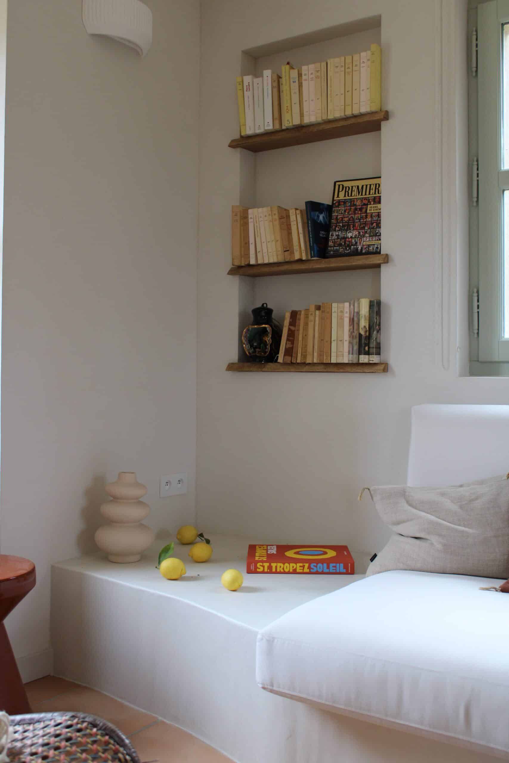 Coin lecture minimaliste avec étagères encastrées, livre St. Tropez Soleil, citrons frais et vase design beige.