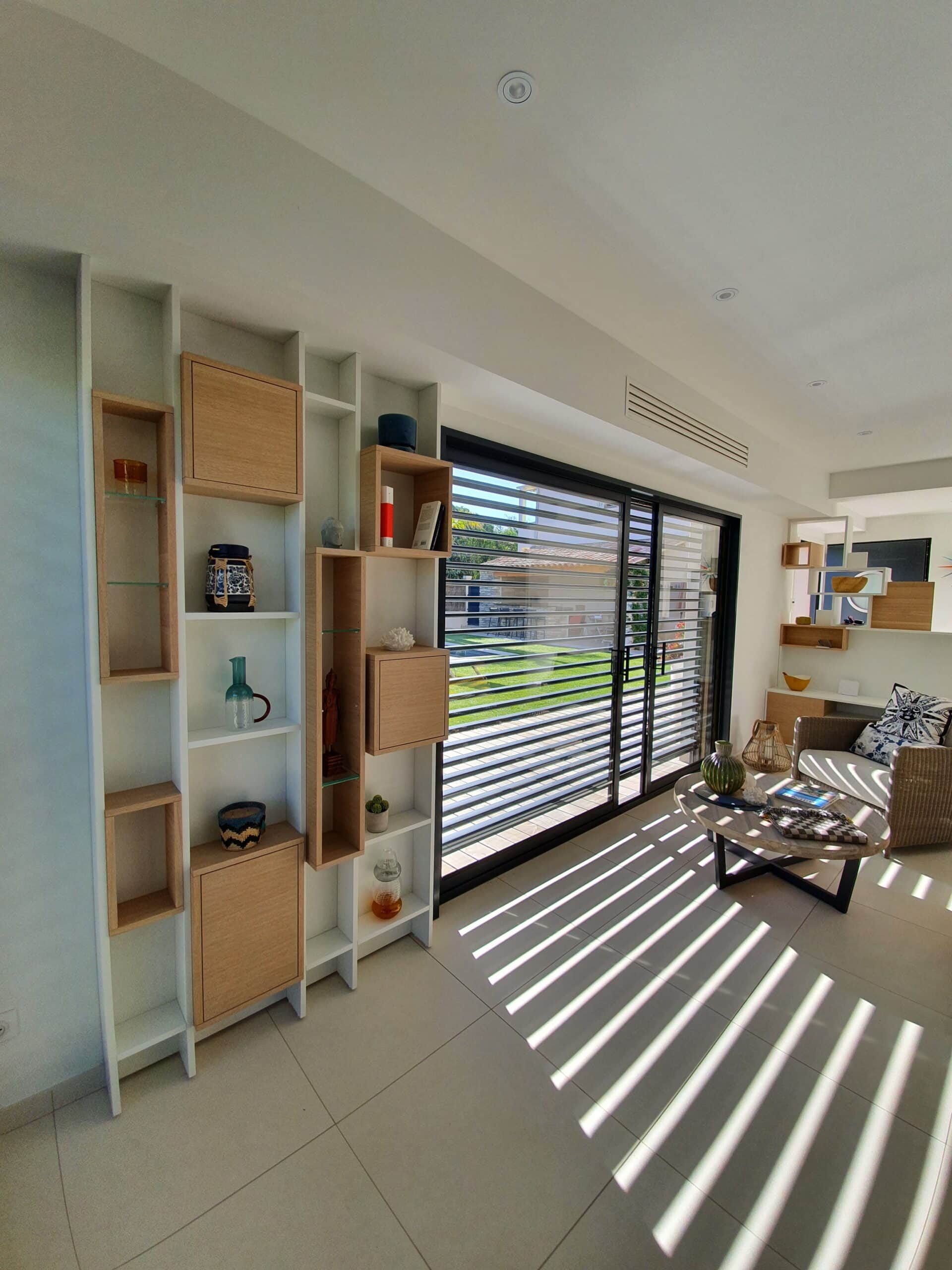 Salon lumineux avec étagère murale bois et blanc, baie vitrée et ombres graphiques au sol.