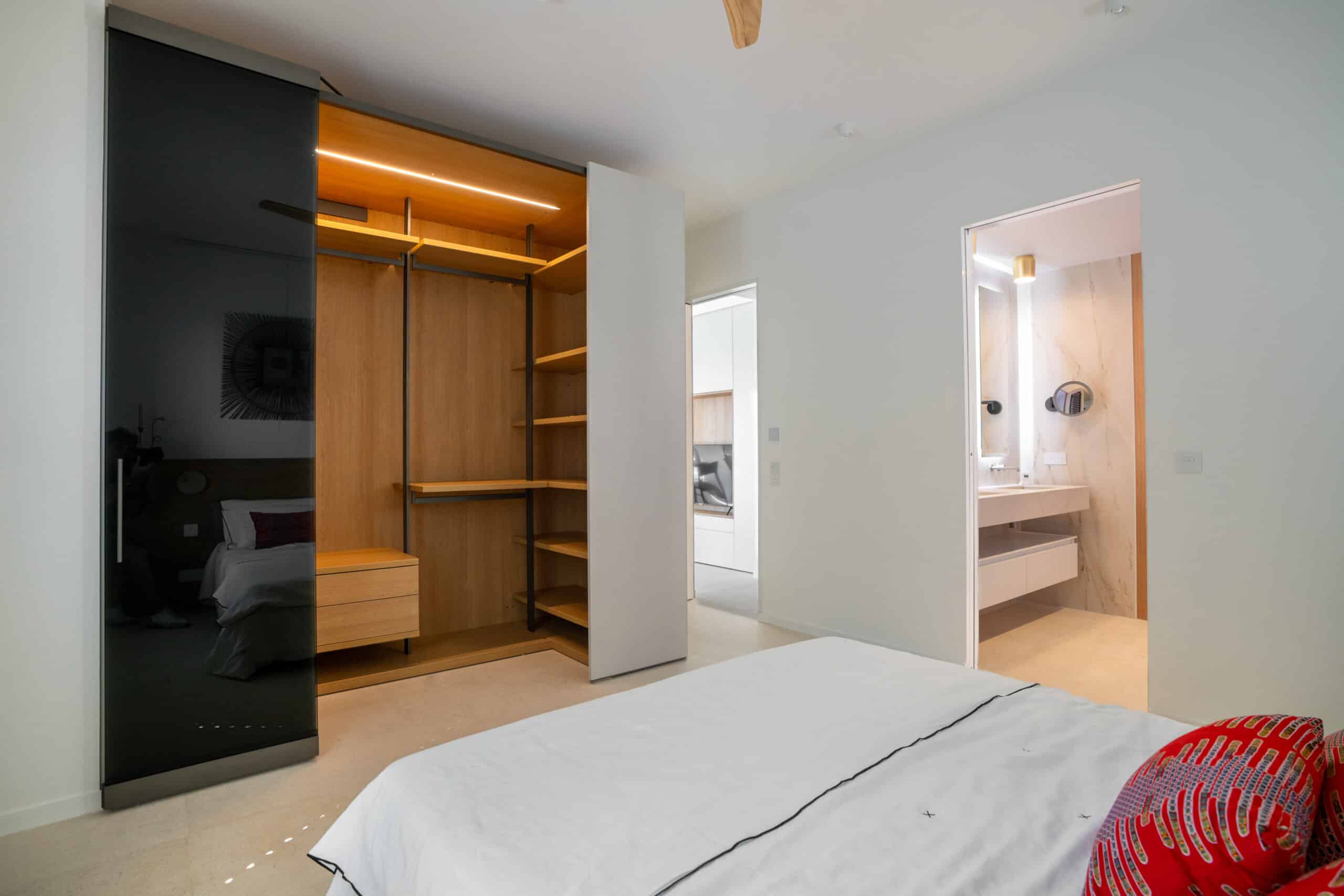 Chambre moderne : dressing bois et verre noir, lit blanc, vue salle de bain attenante lumineuse.