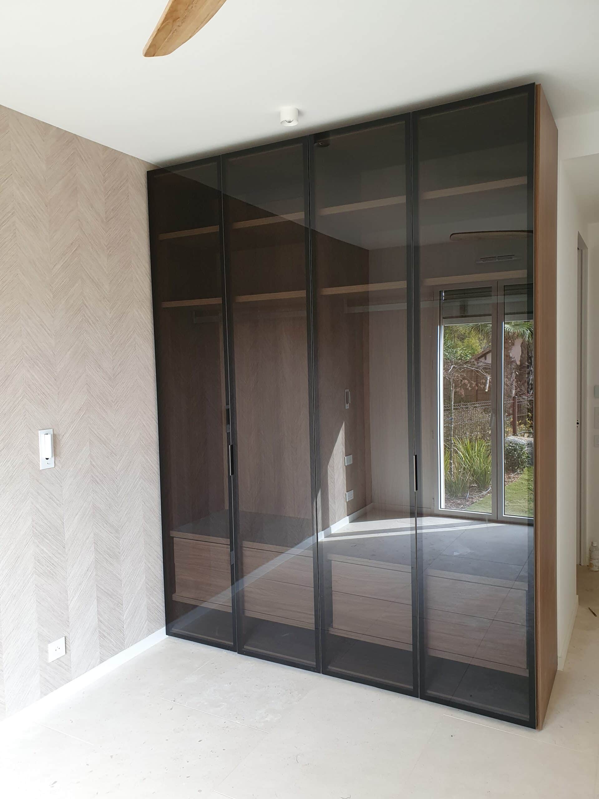 Armoire moderne à portes en verre fumé et cadres noirs, intérieur bois sur mesure.