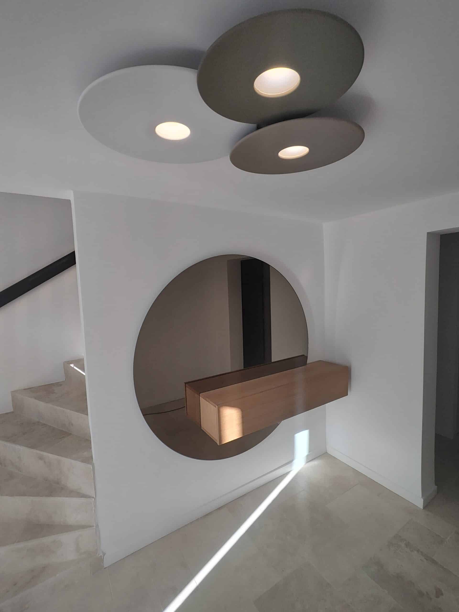 Hall d'entrée moderne avec miroir rond, console flottante en bois et luminaires circulaires design.