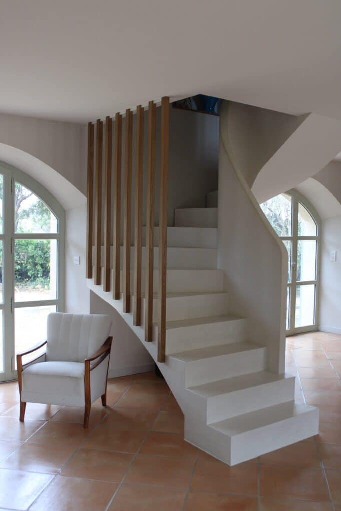 Escalier Design Blanc et Bois | Intérieur Moderne Escalier blanc moderne avec tasseaux bois, fauteuil blanc et sol en terre cuite près de fenêtres cintrées.