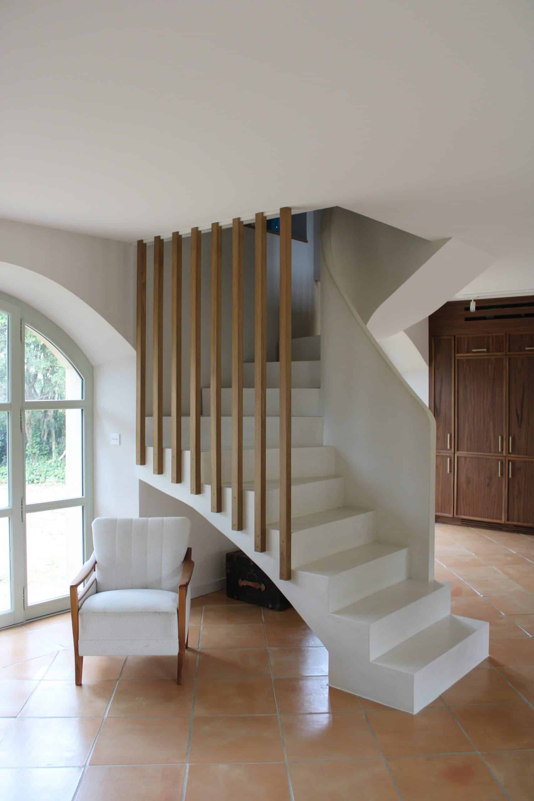 Escalier blanc design avec lattes en bois, fauteuil et sol en terre cuite.