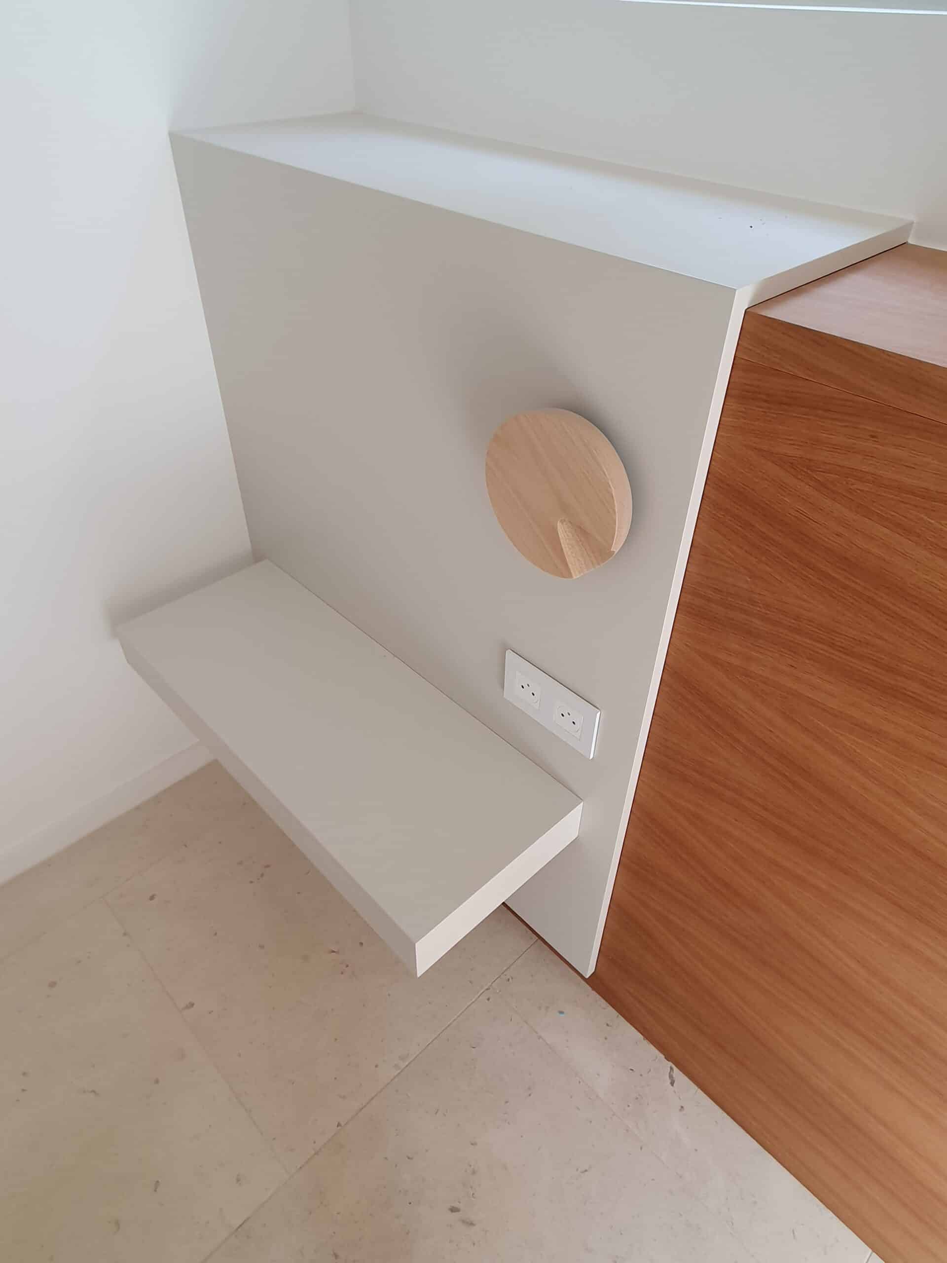 Étagère flottante blanche, applique ronde en bois et prise de courant sur mur gris minimaliste.