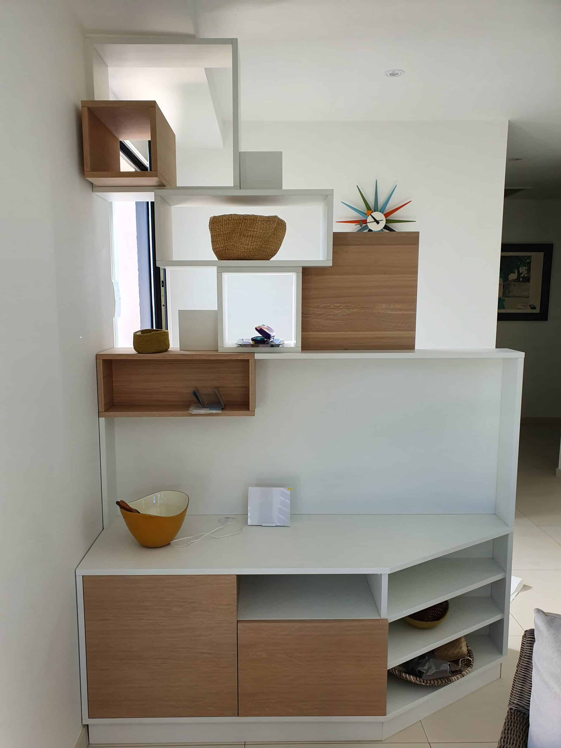 Étagère modulaire blanc et bois asymétrique avec objets déco et horloge colorée.