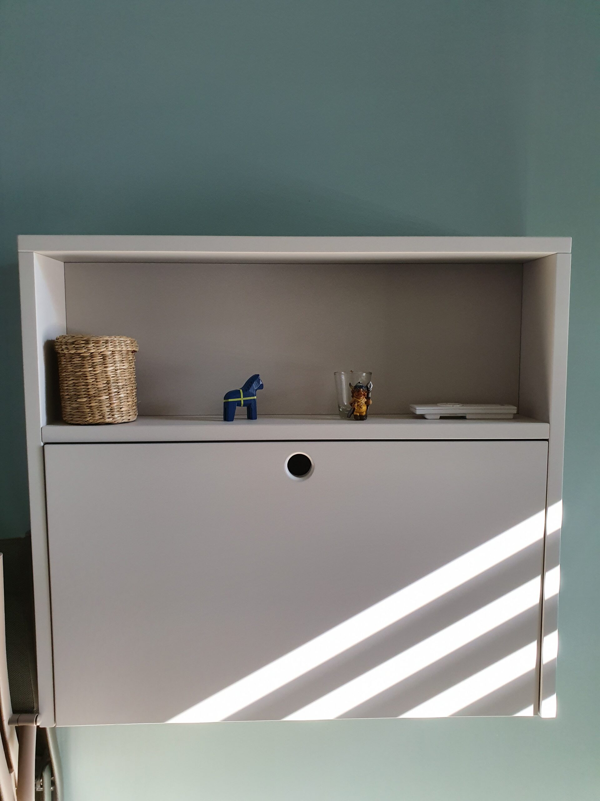 Étagère murale blanche avec panier osier, cheval Dala bleu et figurines sous des ombres de lumière naturelle.