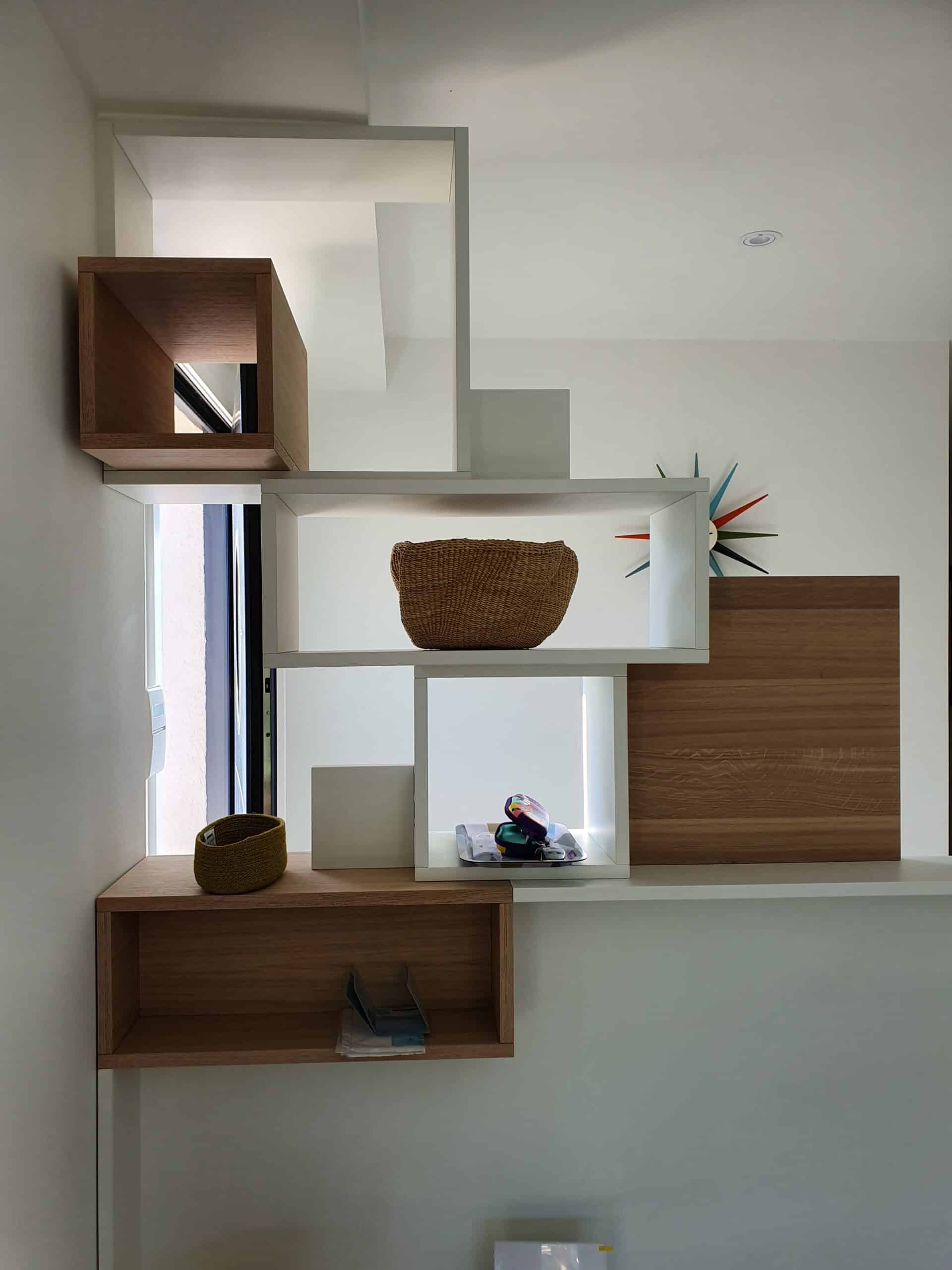 Étagère murale asymétrique blanche et bois avec panier en osier et horloge colorée.