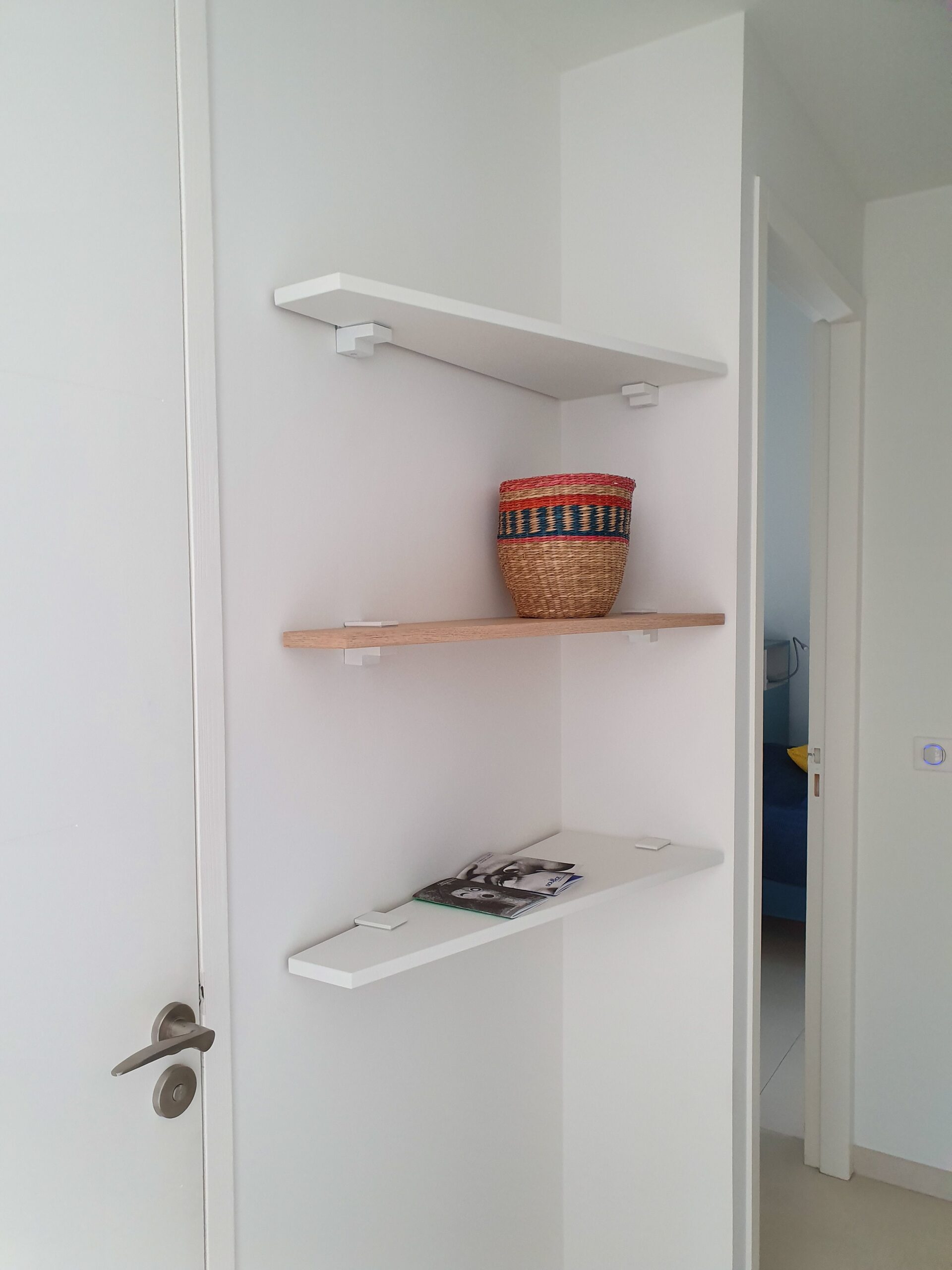 Étagères murales d'angle avec panier tressé coloré et livre dans un intérieur blanc moderne.