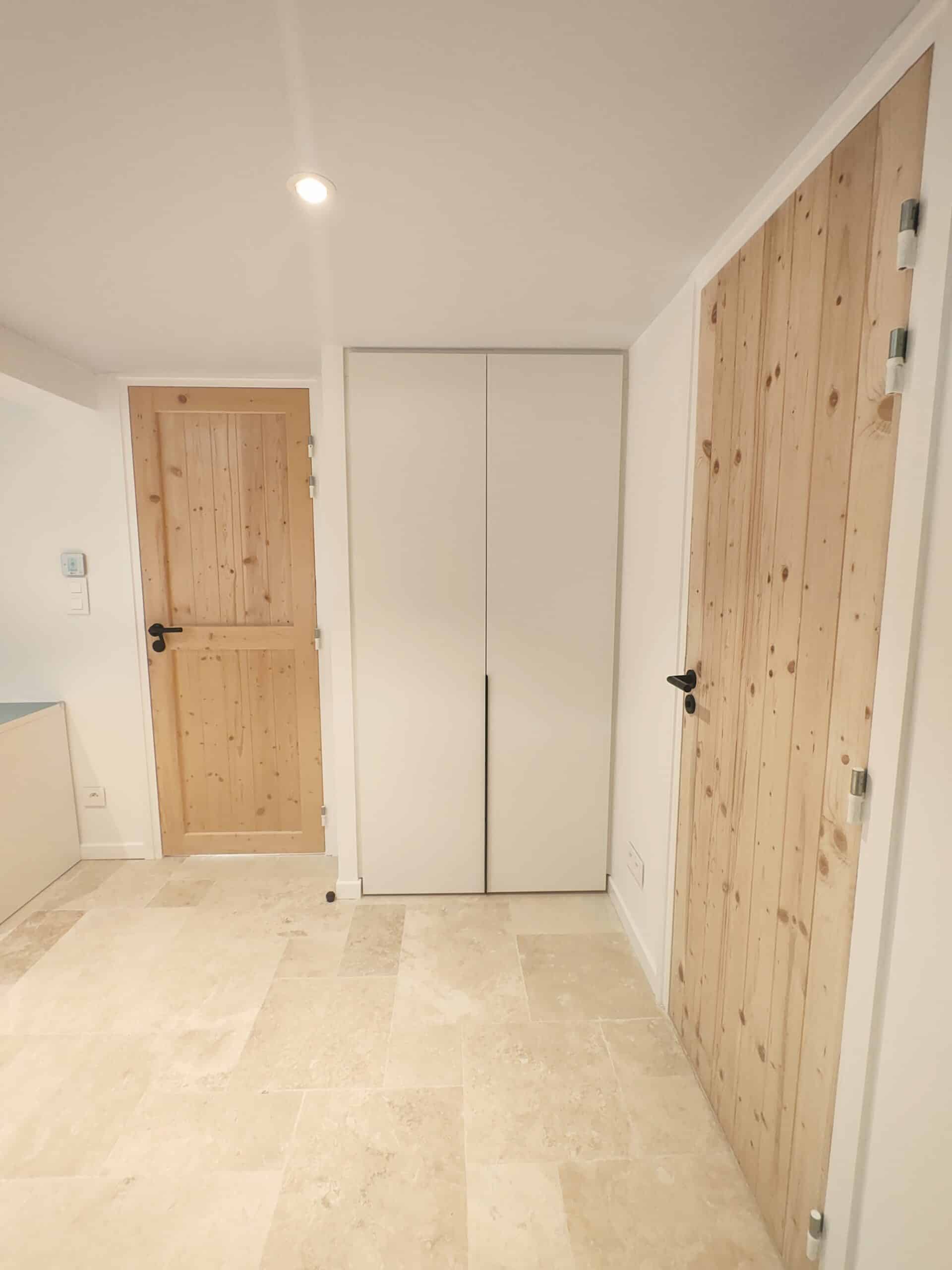Hall avec portes en bois clair, placard blanc et sol en travertin.