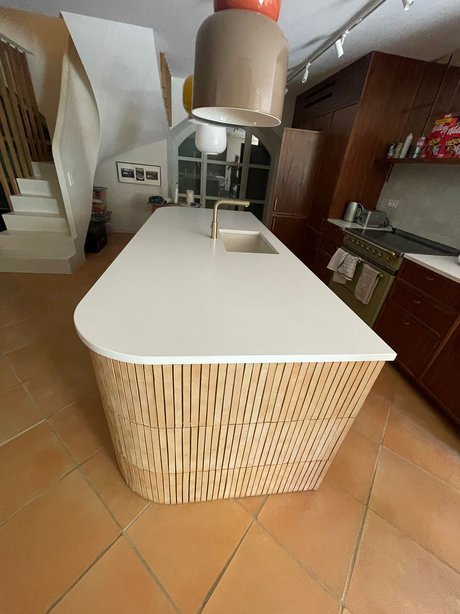 Îlot de cuisine avec plan blanc courbé, base à lattes en bois clair et carrelage en terre cuite.