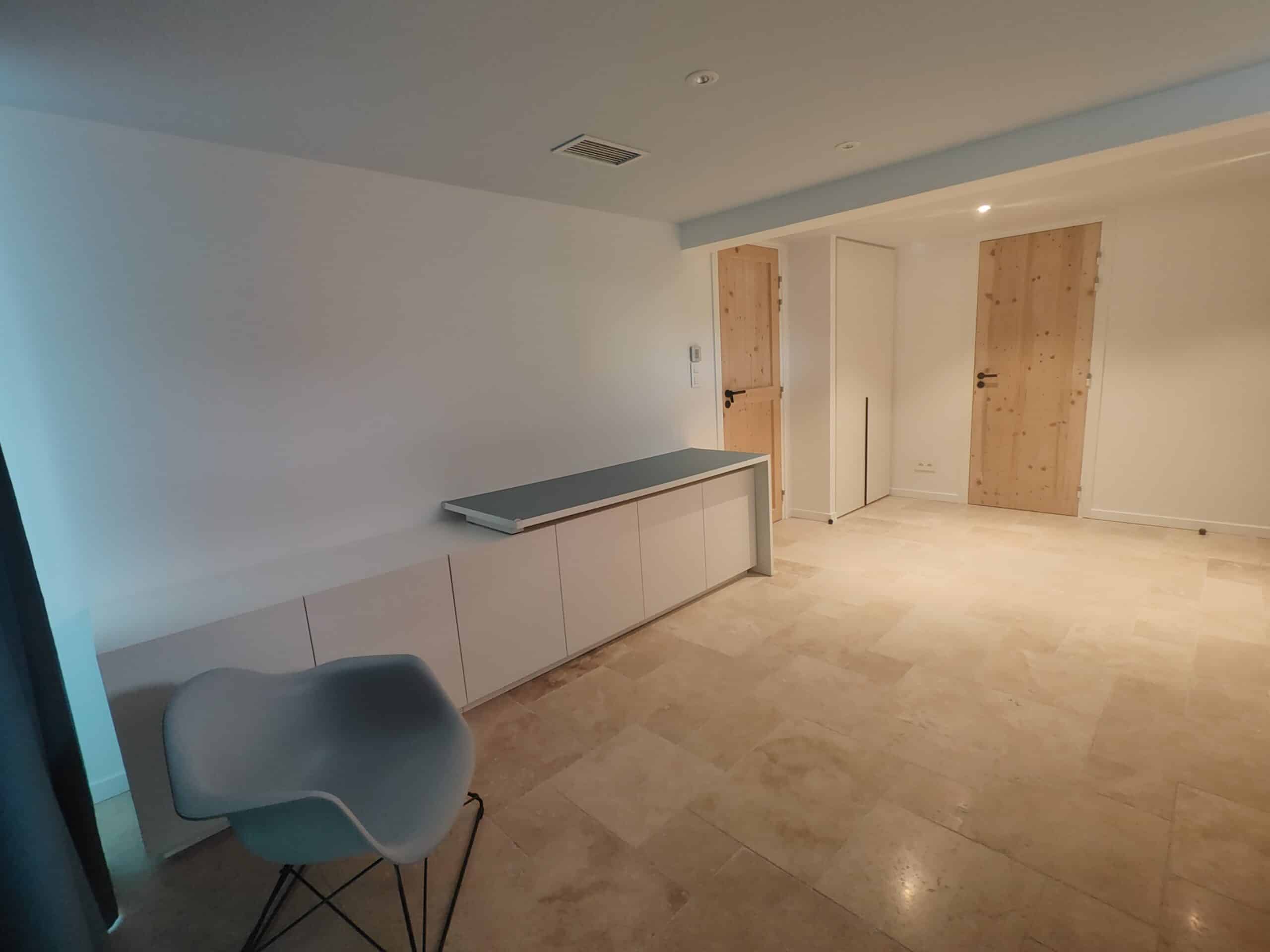Salon moderne avec buffet blanc, chaise design grise, sol en travertin et portes en bois clair.