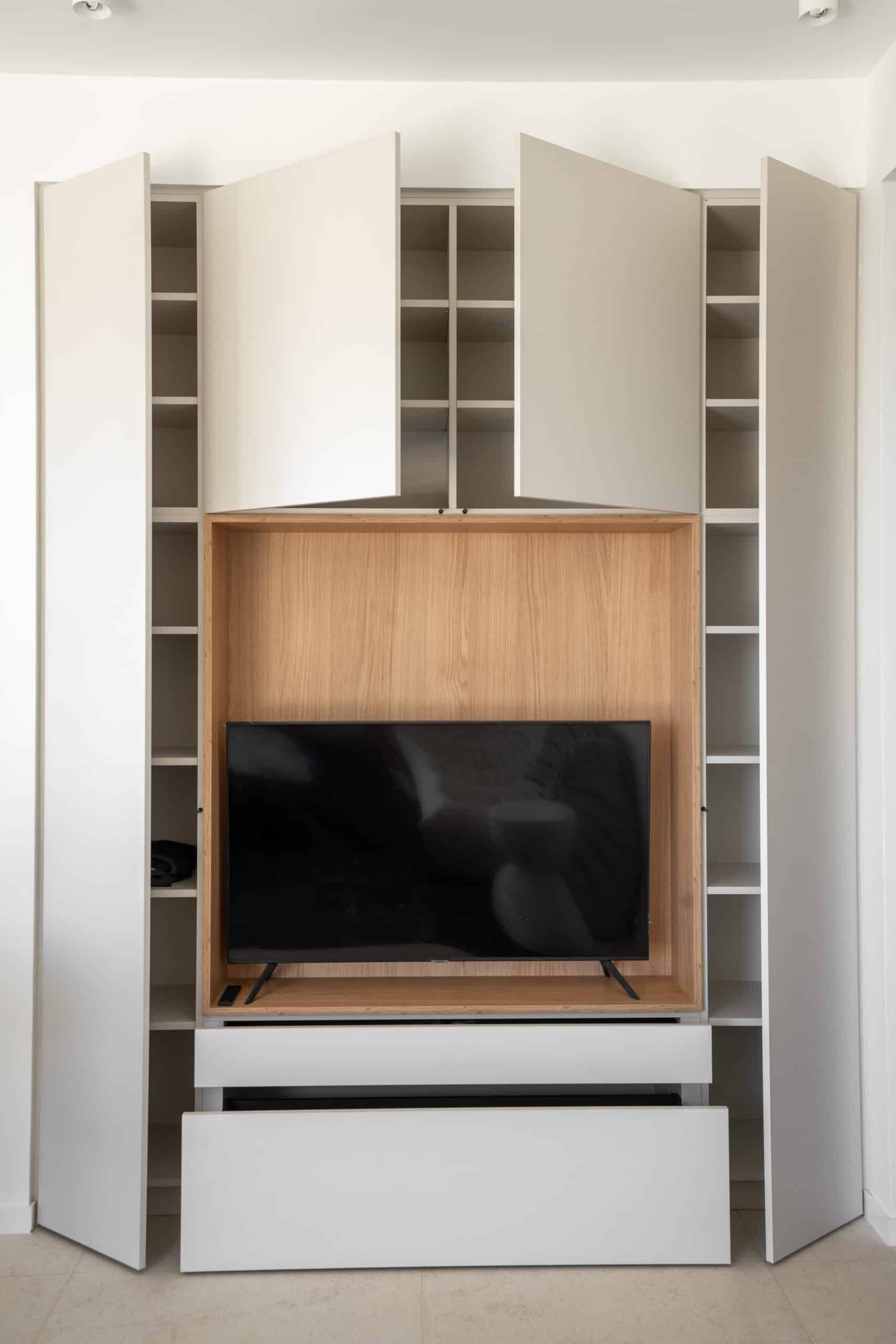 Meuble TV sur mesure blanc avec niche en bois clair, portes pliantes et rangements minimalistes intégrés.