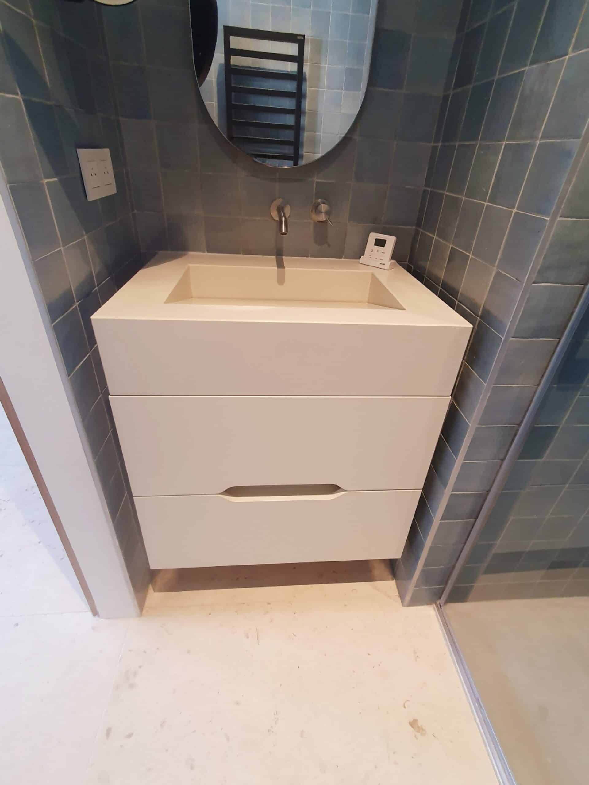 Vasque blanche suspendue sur carrelage bleu avec miroir rond et robinet mural.
