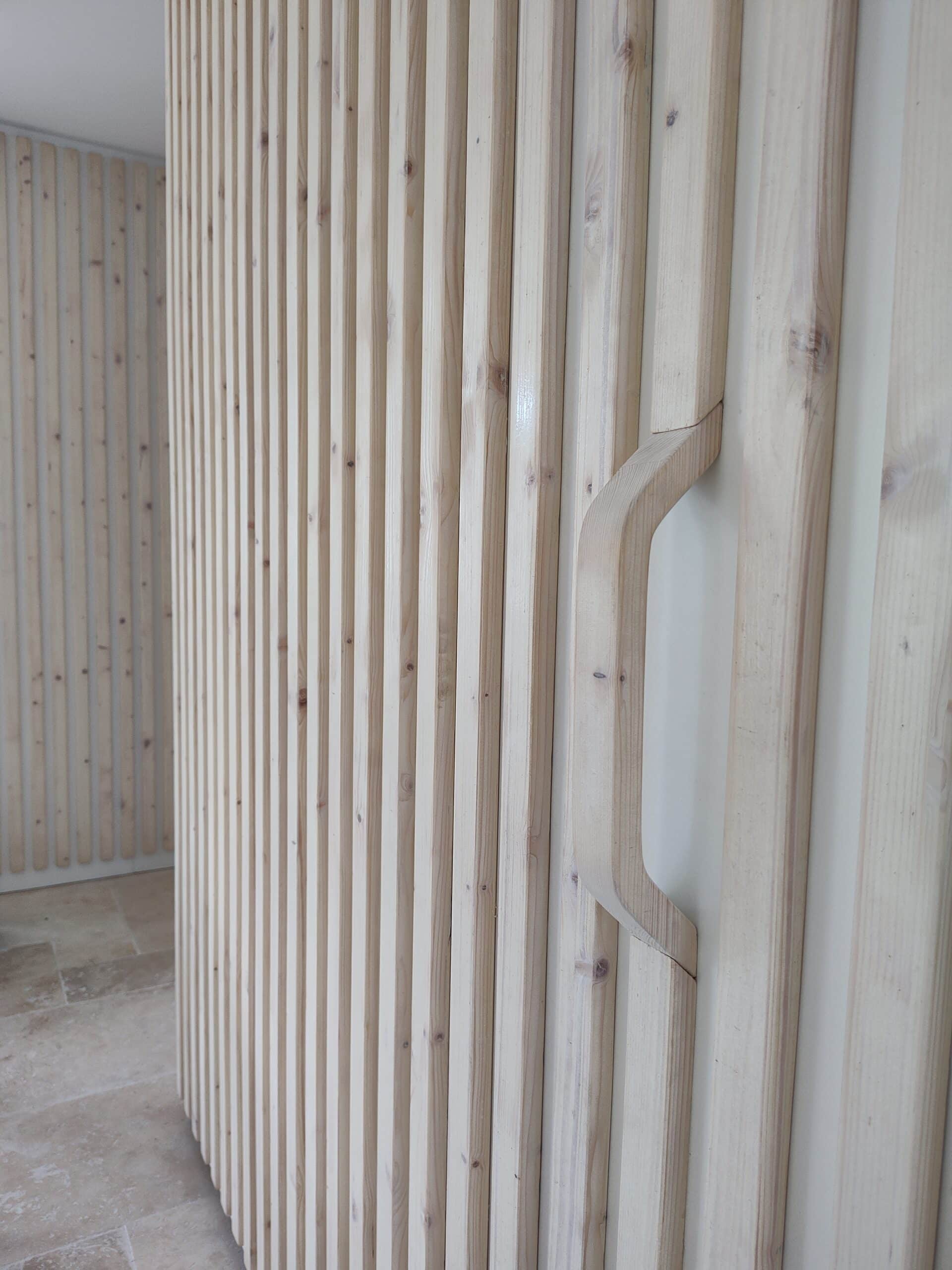 Mur en tasseaux bois clair avec poignée intégrée design minimaliste.