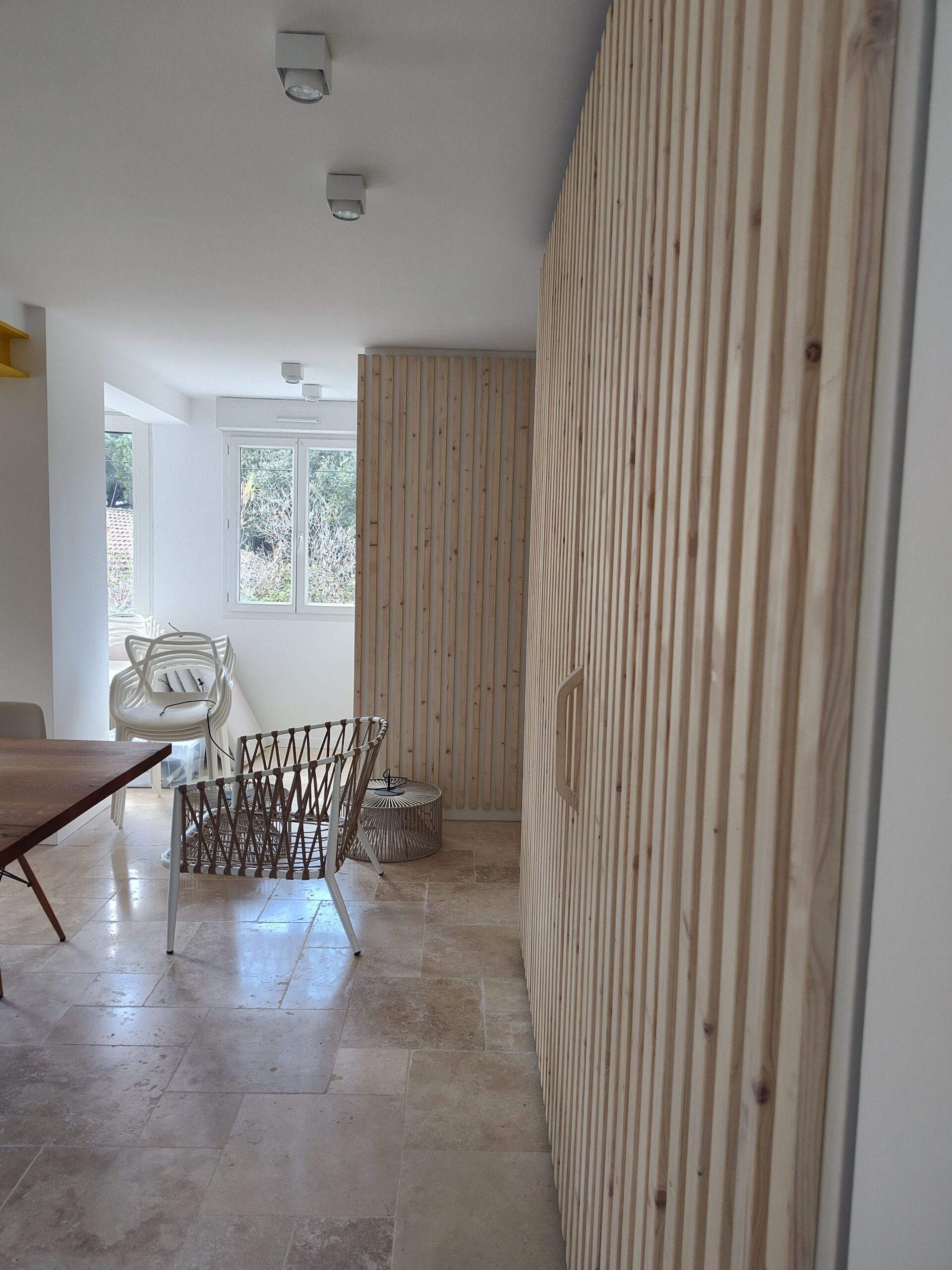 Intérieur moderne avec mur en tasseaux de bois clair, sol en travertin et fauteuil tressé design.