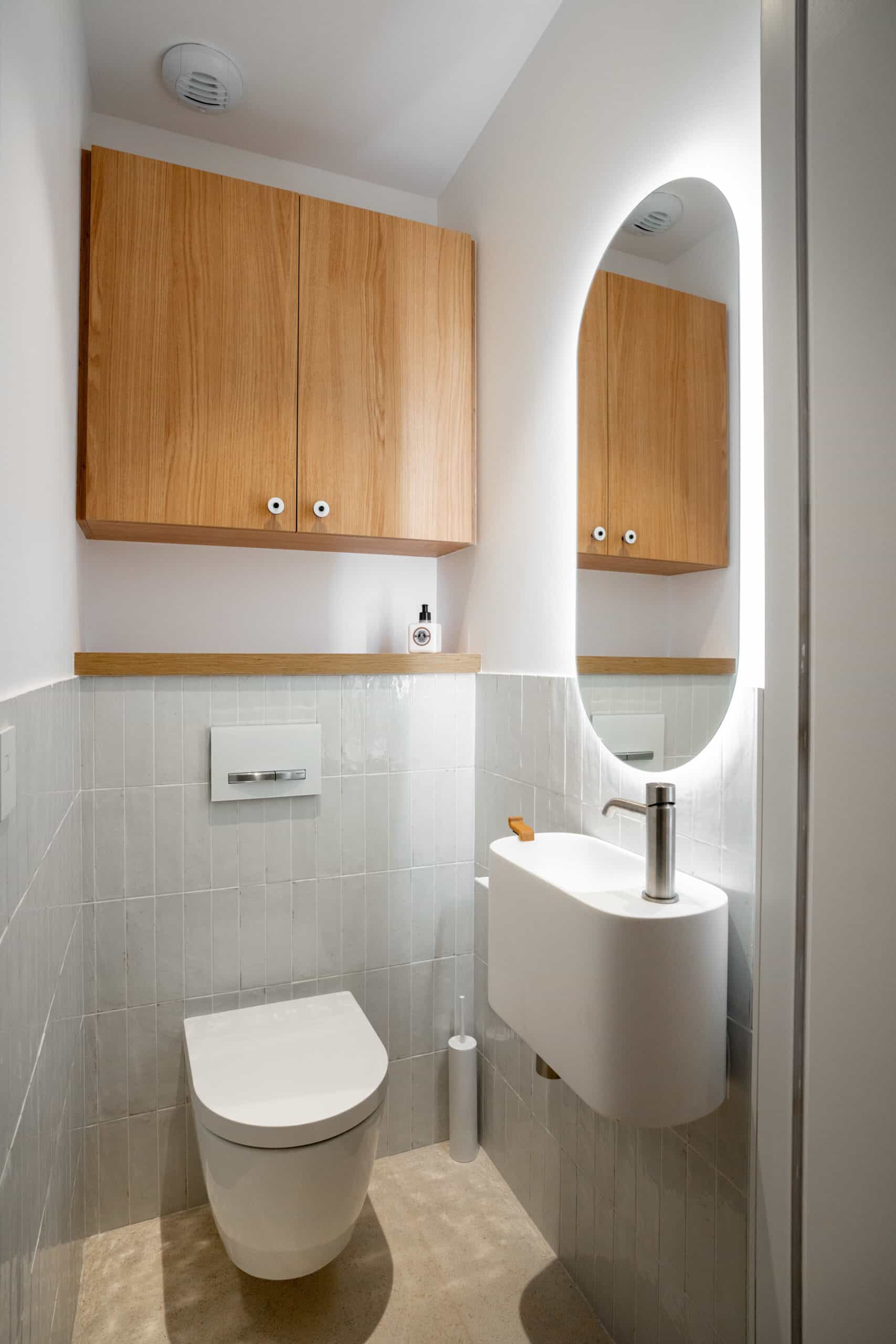 Petit WC moderne : toilettes suspendues, lavabo compact, miroir rétroéclairé et placard en bois.