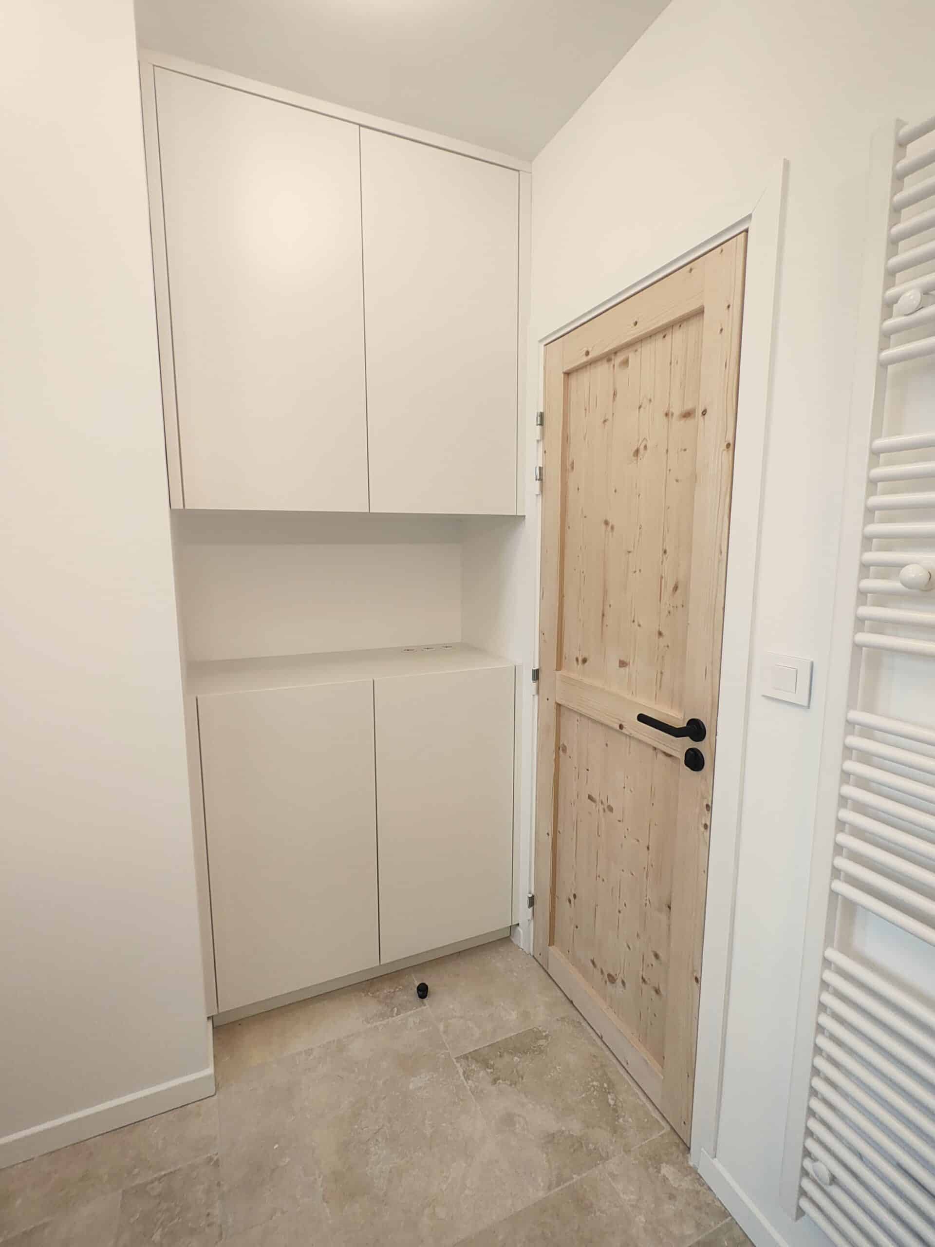 Placard blanc encastré, porte en bois clair et sèche-serviette blanc sur carrelage beige.
