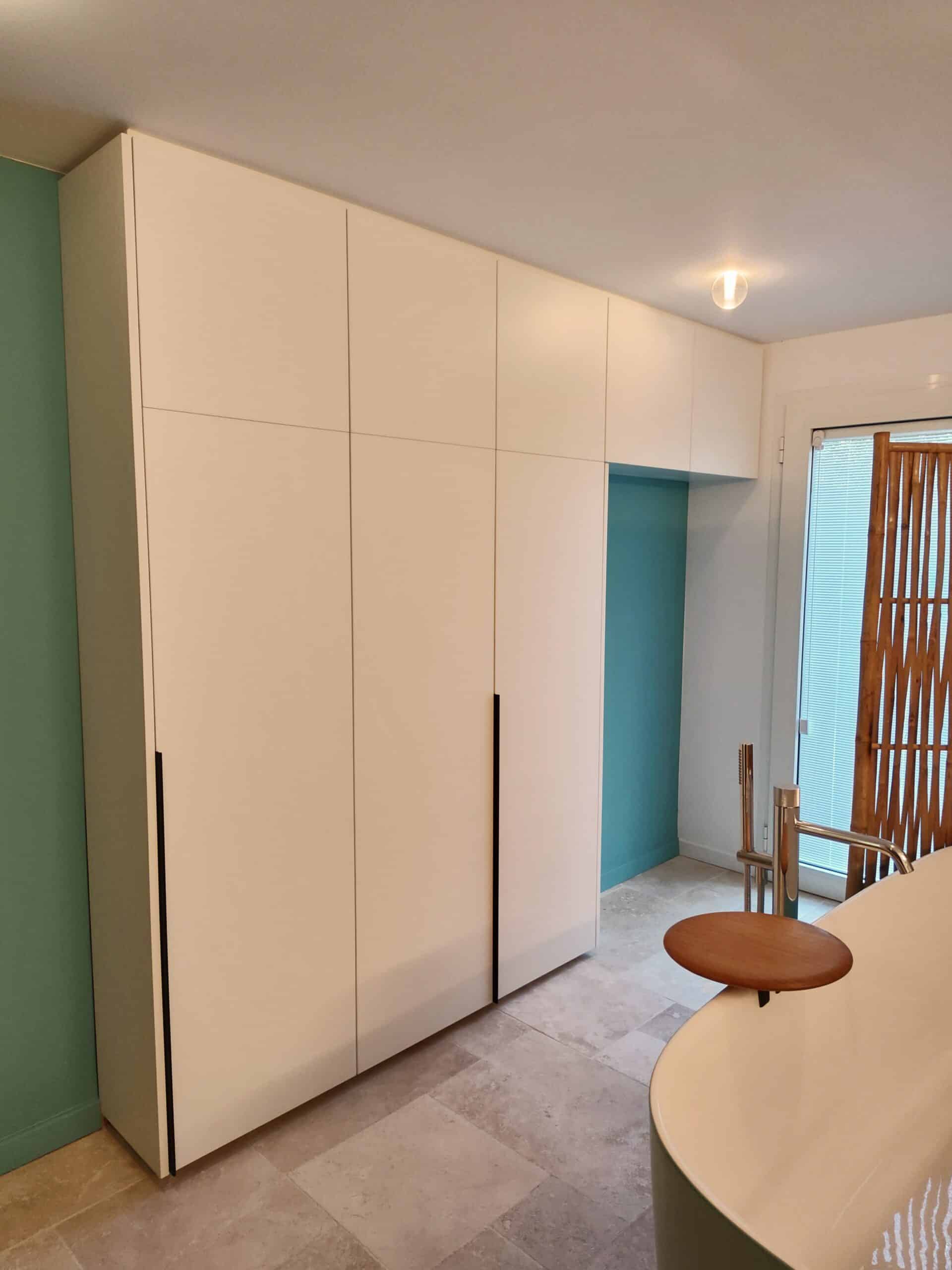 Placard blanc minimaliste, mur bleu canard et baignoire design dans une salle de bain moderne.
